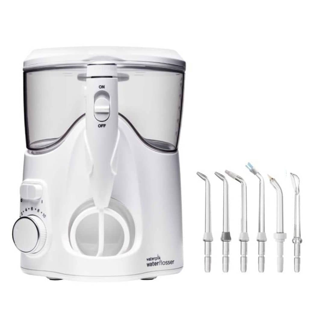 Un irrigador bucal Waterpik blanco con varias puntas a la derecha. Tiene un interruptor de encendido/apagado y un dial.