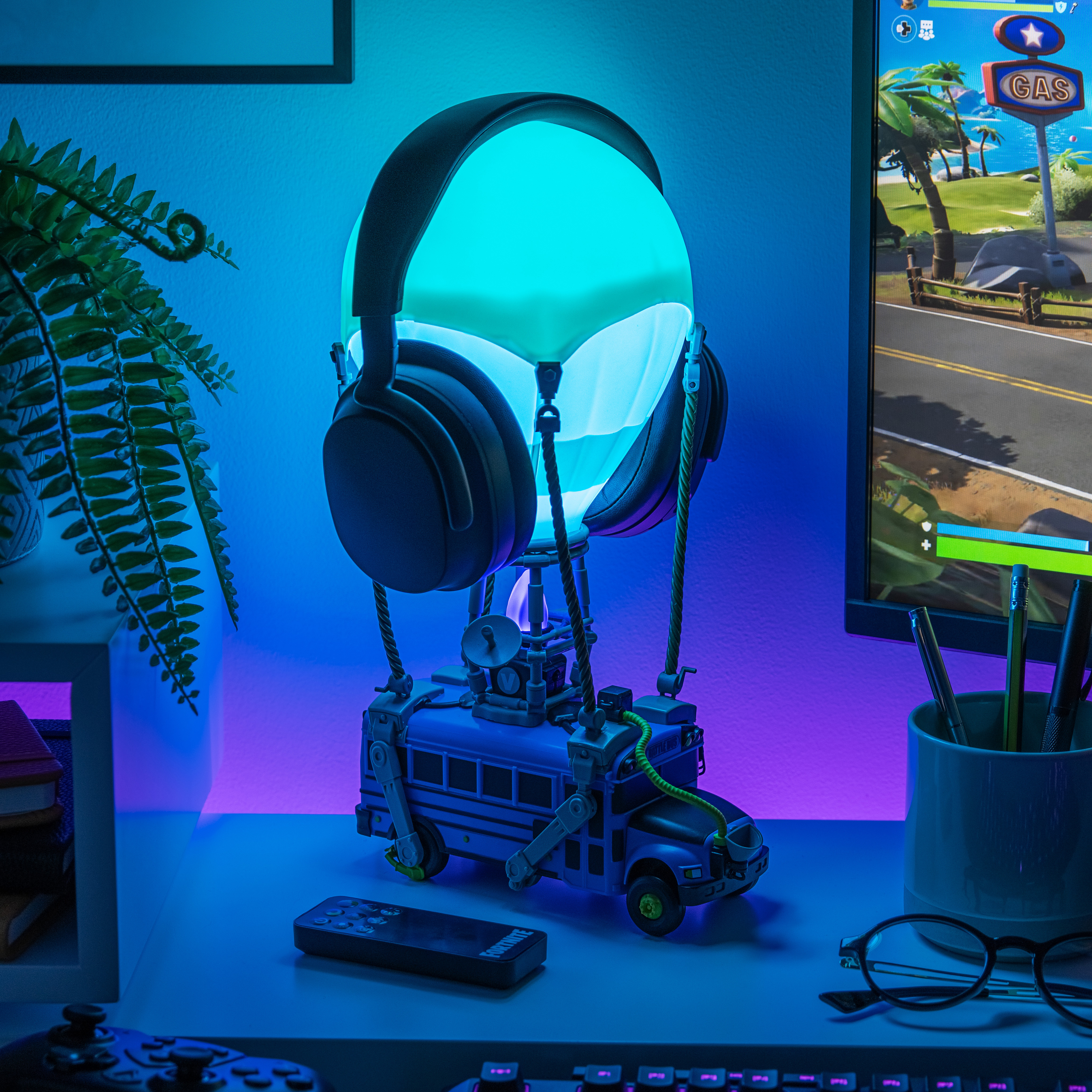 Eine Fortnite Battle Bus-Lampe mit Kopfhörern, ein Bildschirm mit einem Spiel und anderem Gaming-Zubehör.