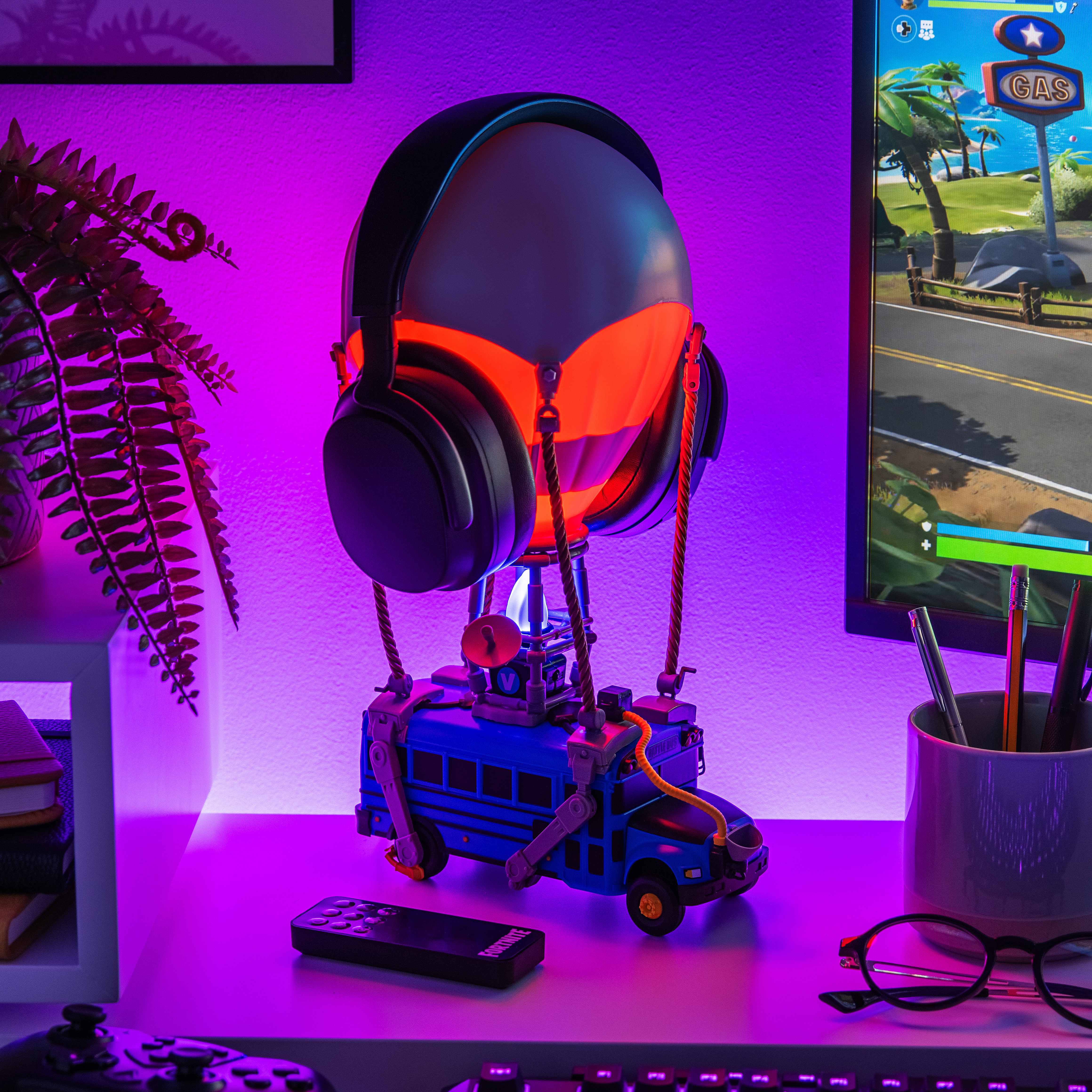 Ein Fortnite-Spielzeug vor einem Monitor, der das Spiel anzeigt. Kopfhörer sind oben. Lila Licht.