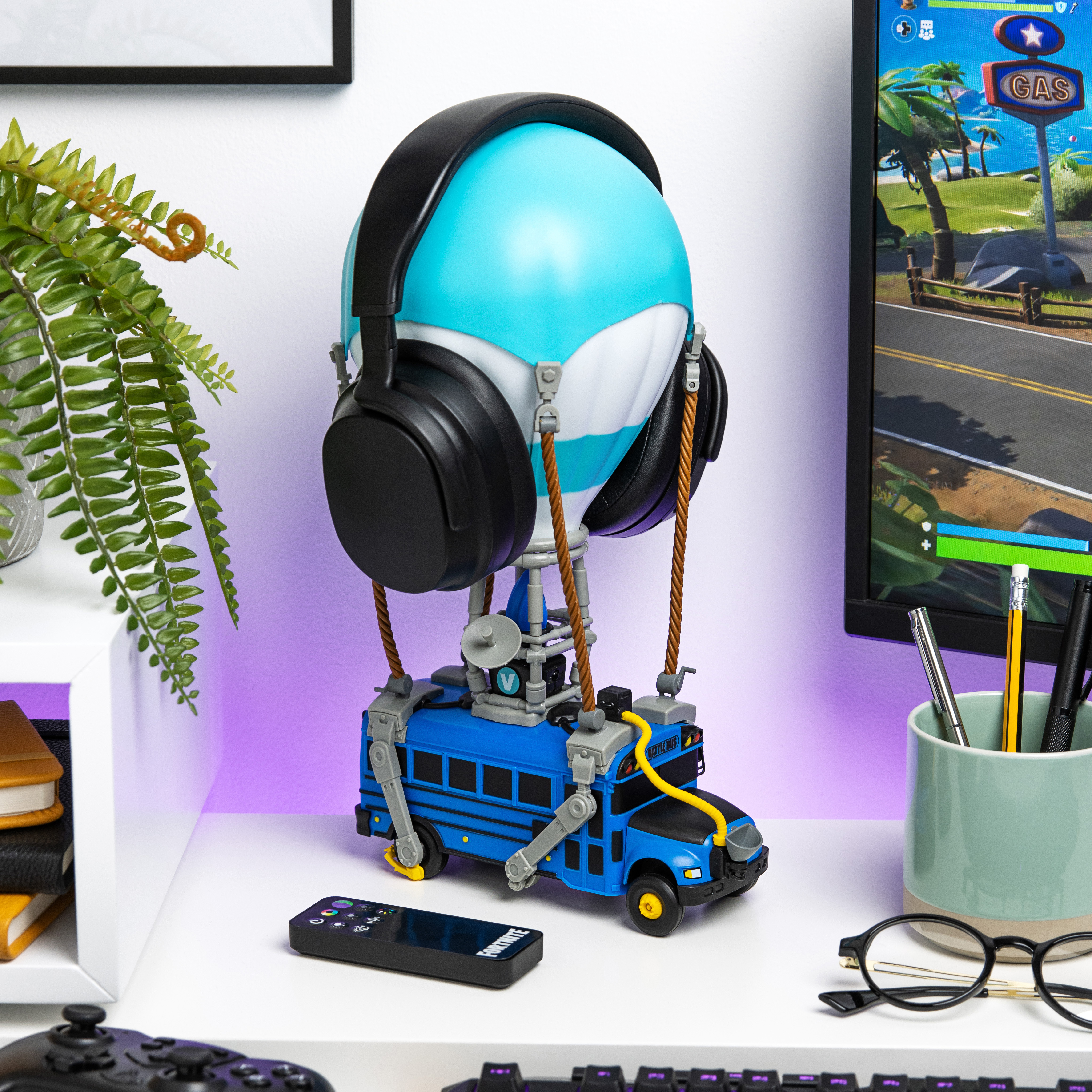 Ein Fortnite-Spielzeug vor einem Computer. Es hat Kopfhörer, ein blaues Busmodell und eine Fernbedienung.