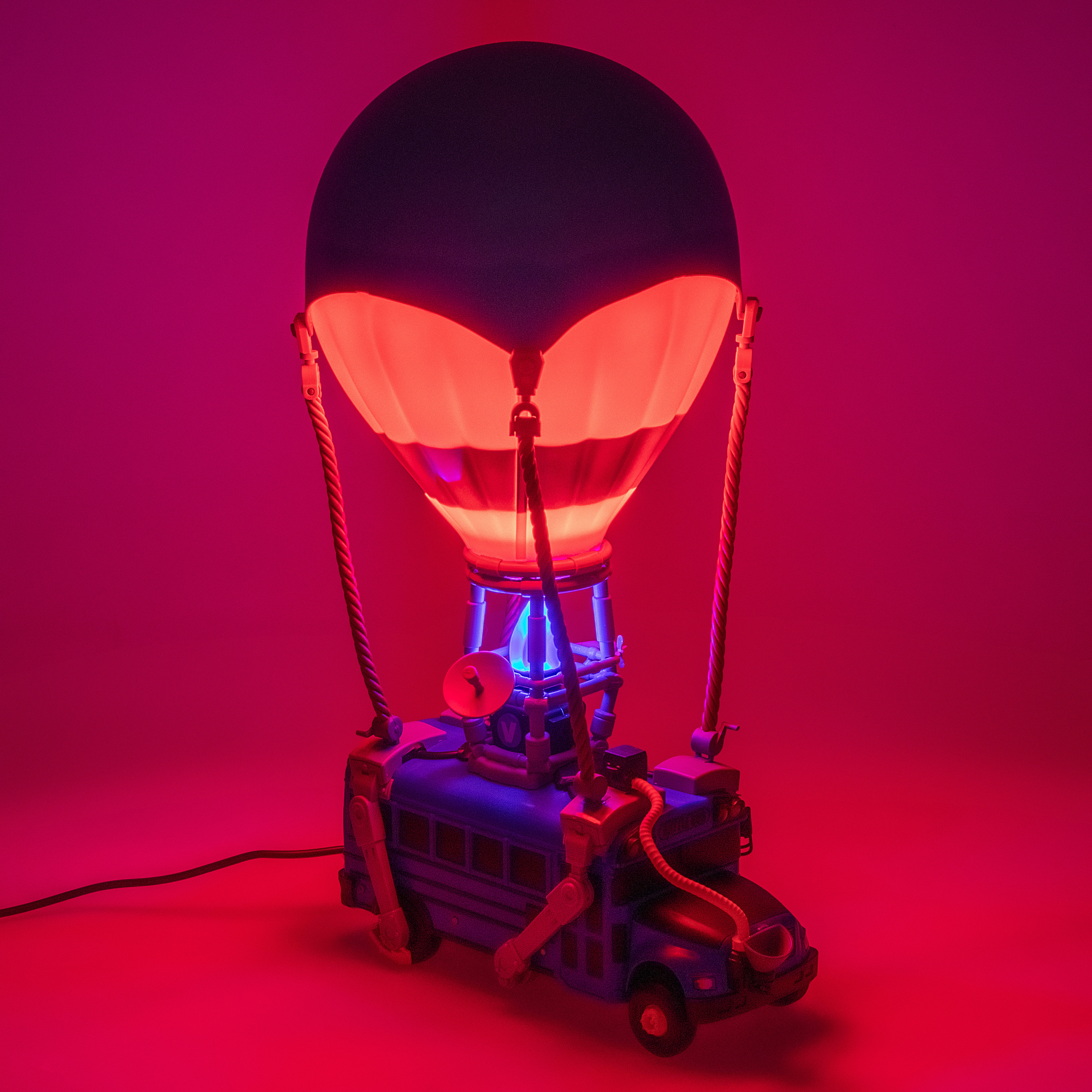 Eine Lampe in Form eines Heißluftballons über einem blauen Bus. Rote und violette Beleuchtung erzeugt einen dramatischen Effekt.