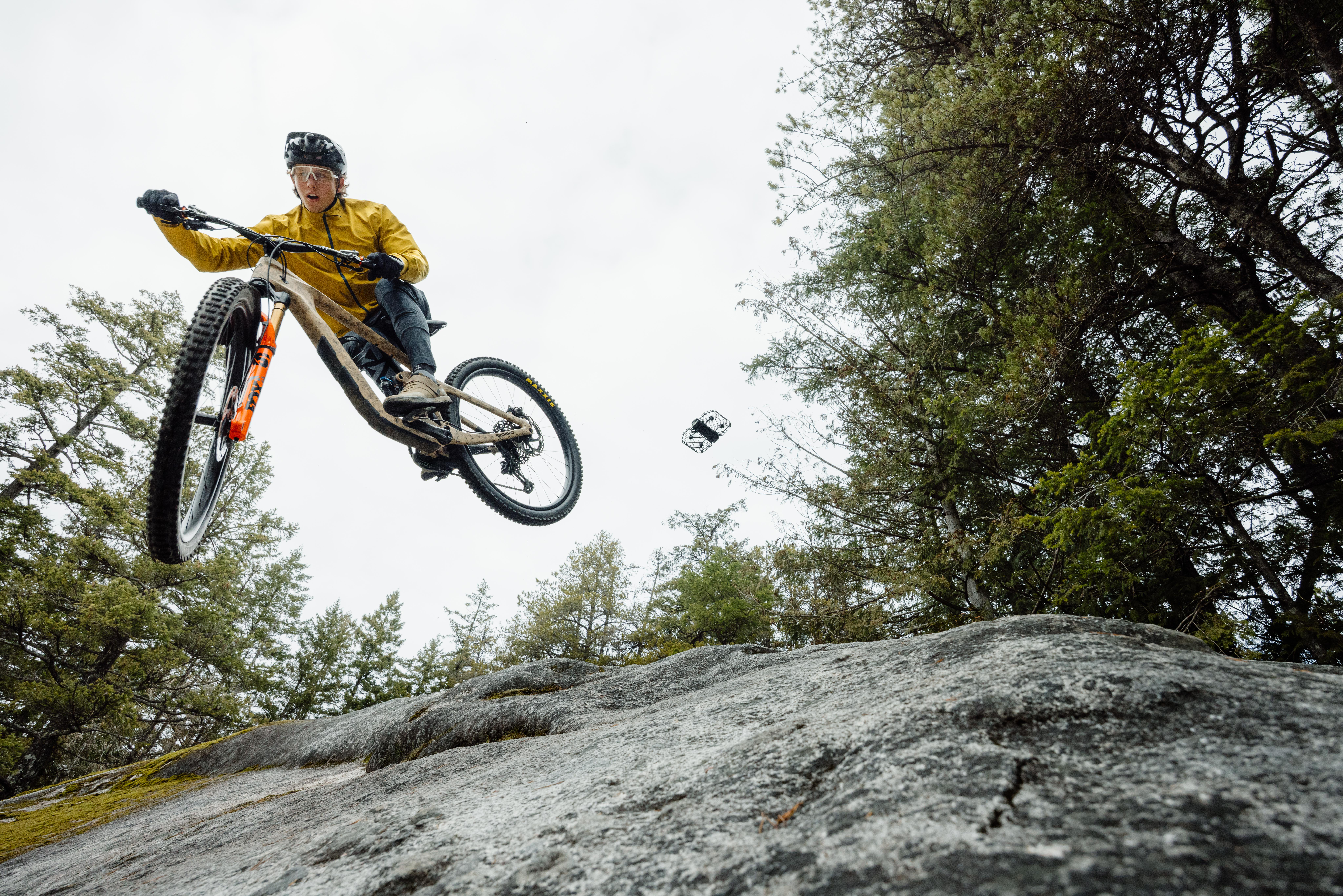 Ein Radfahrer springt mit einem Mountainbike, mit Bäumen und einem bewölkten Himmel im Hintergrund.