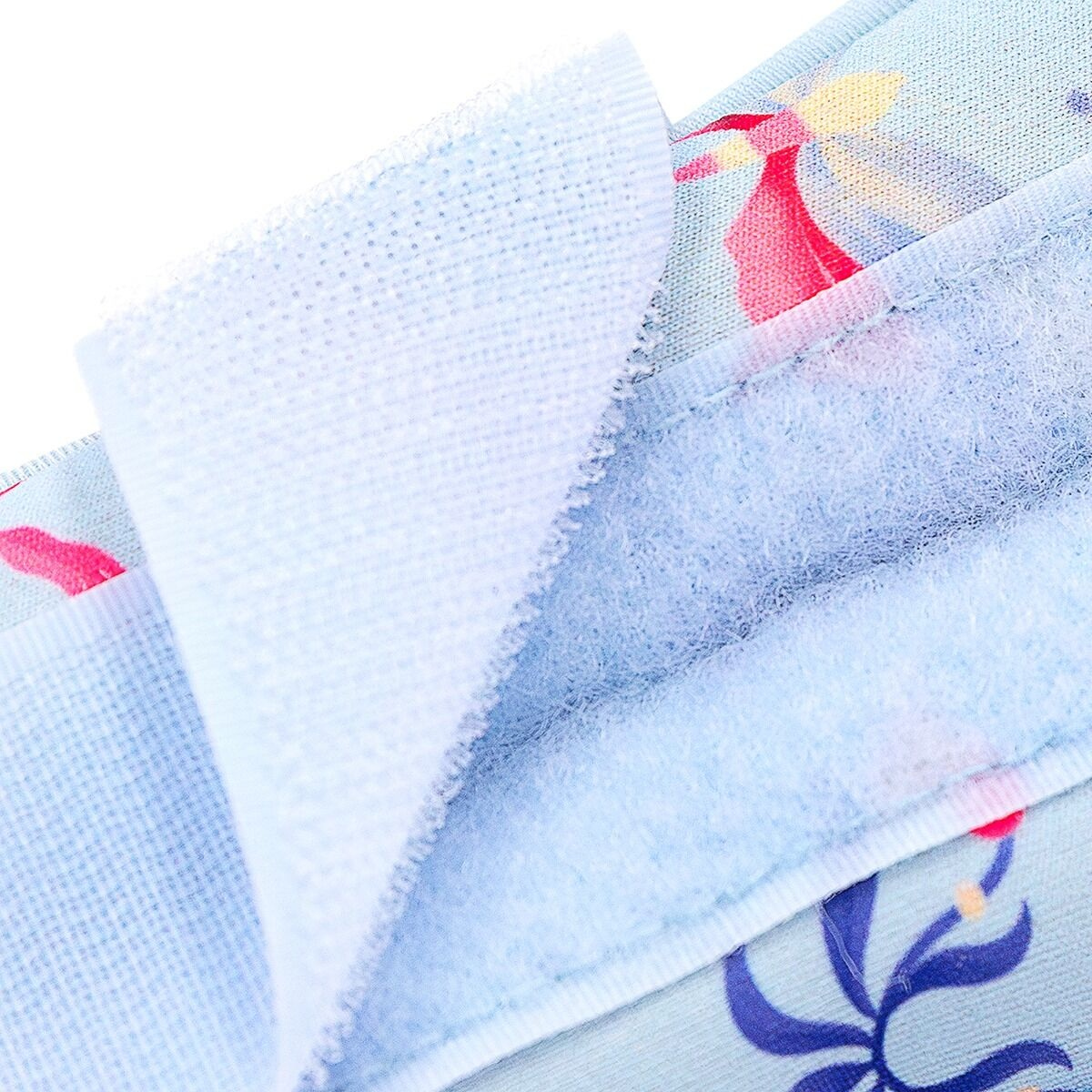 Zbliżenie jasnoniebieskiego materiału z zapięciem na rzep. Materiał ma kwiatowe wzory z czerwonymi i niebieskimi akcentami.