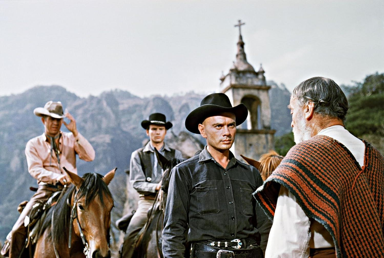 Cowboys auf Pferden stehen einem älteren Mann gegenüber. Im Hintergrund befindet sich eine Kirche. Berge und Himmel vervollständigen die Szene.