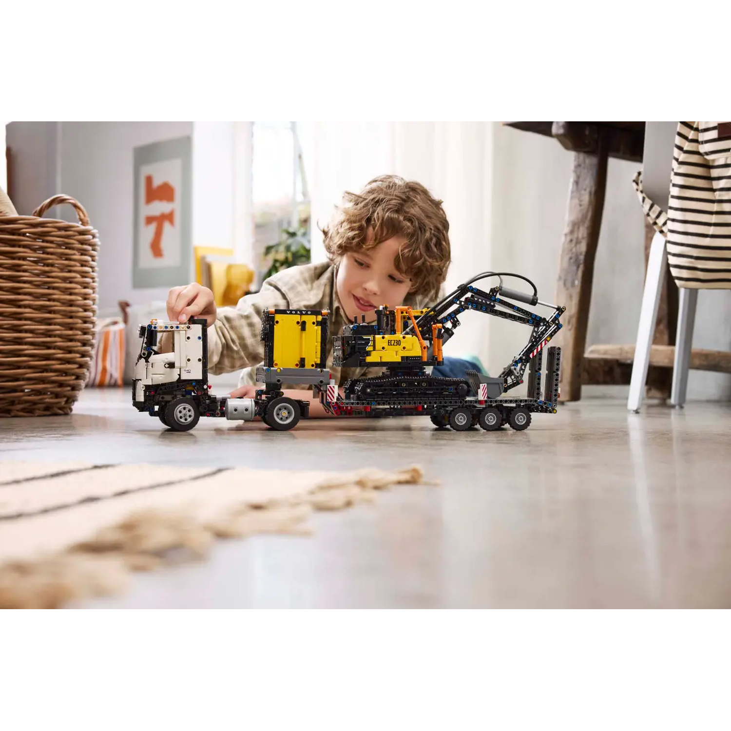 A boy plays with a construction toy, a truck and an excavator. The scene is indoors on a wooden floor.
