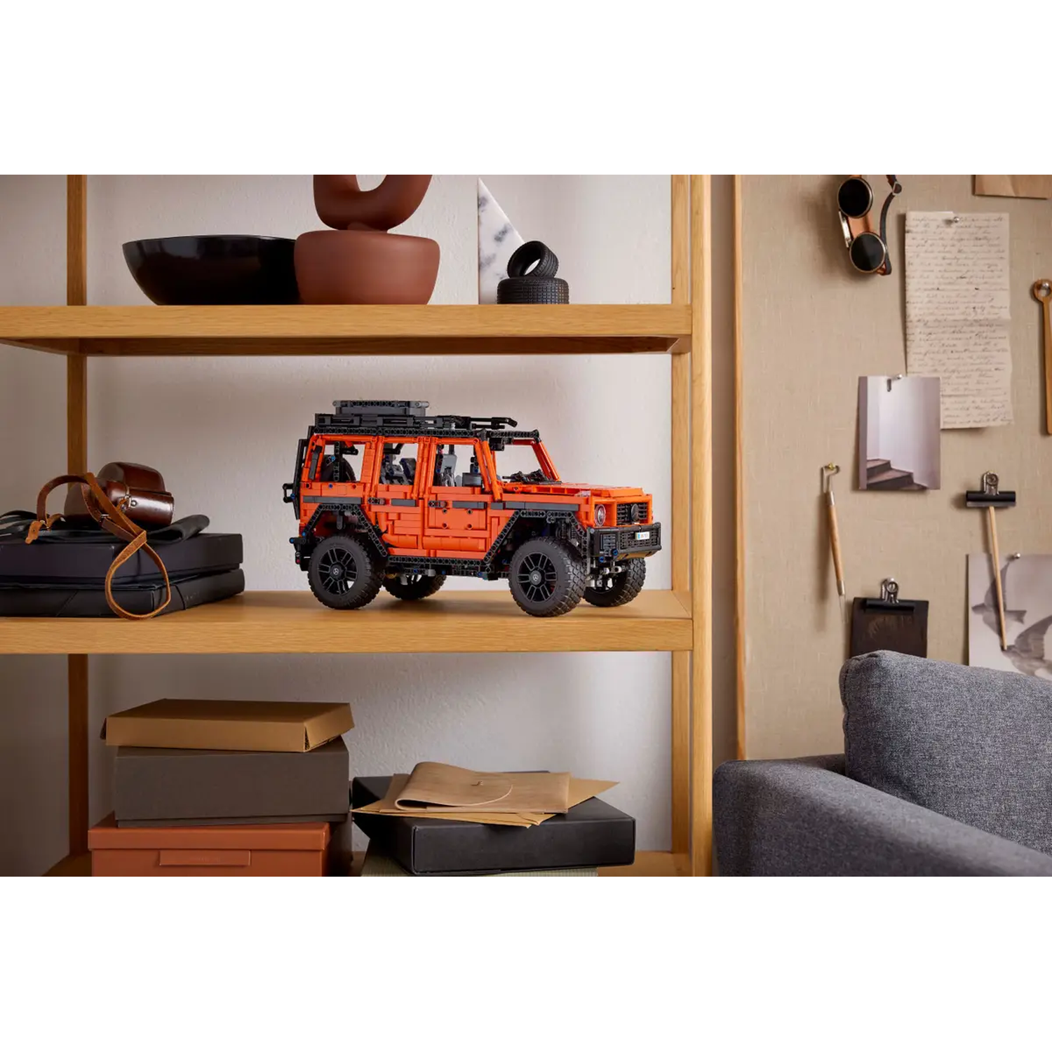 An orange Lego car sits on a shelf. Other items include a black bowl, boxes, and tires. Background shows a wall with items.
