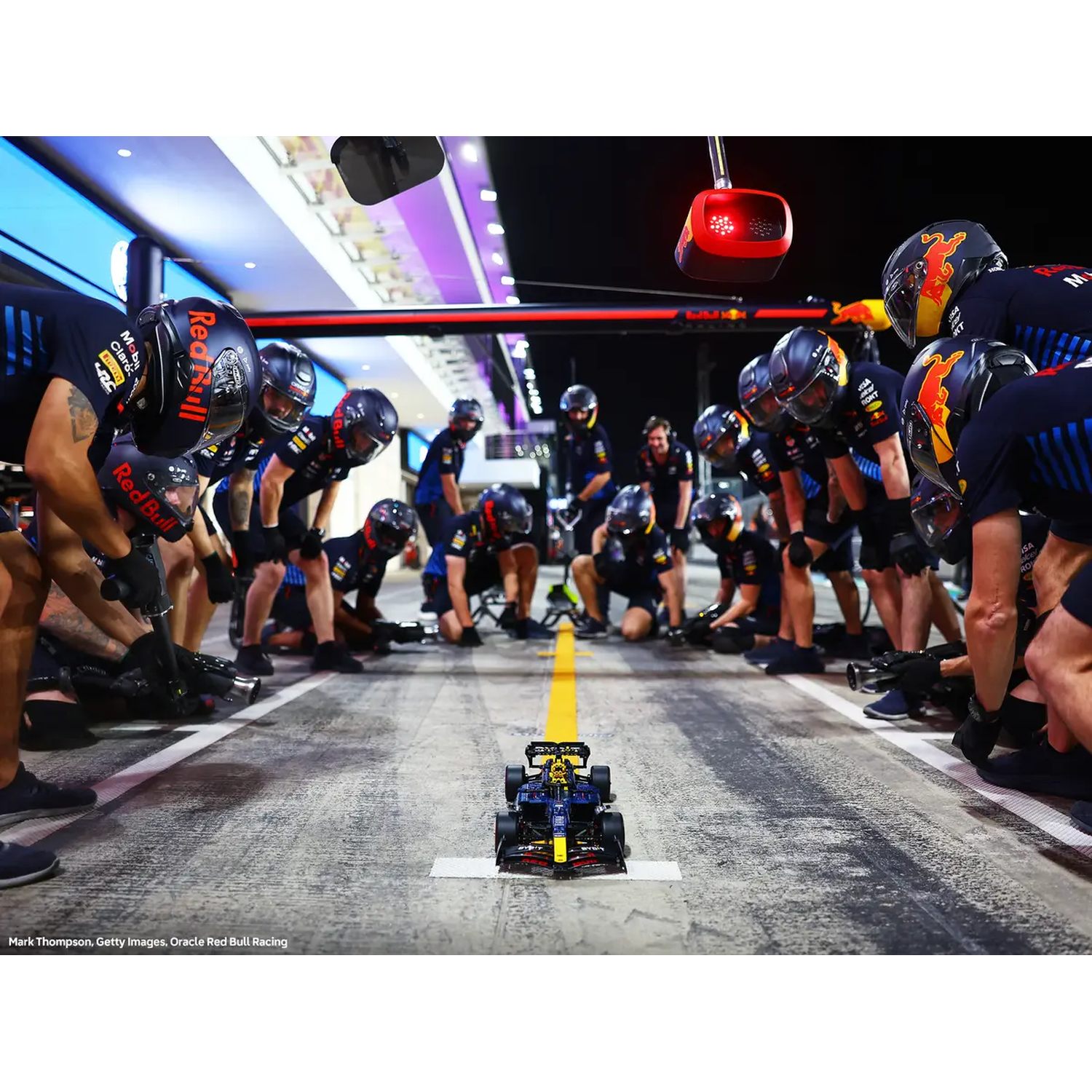 Formule 1 pitstop. Team omringt de auto, klaar. Monteur vooraan. Red Bull auto, gele lijn op de grond.