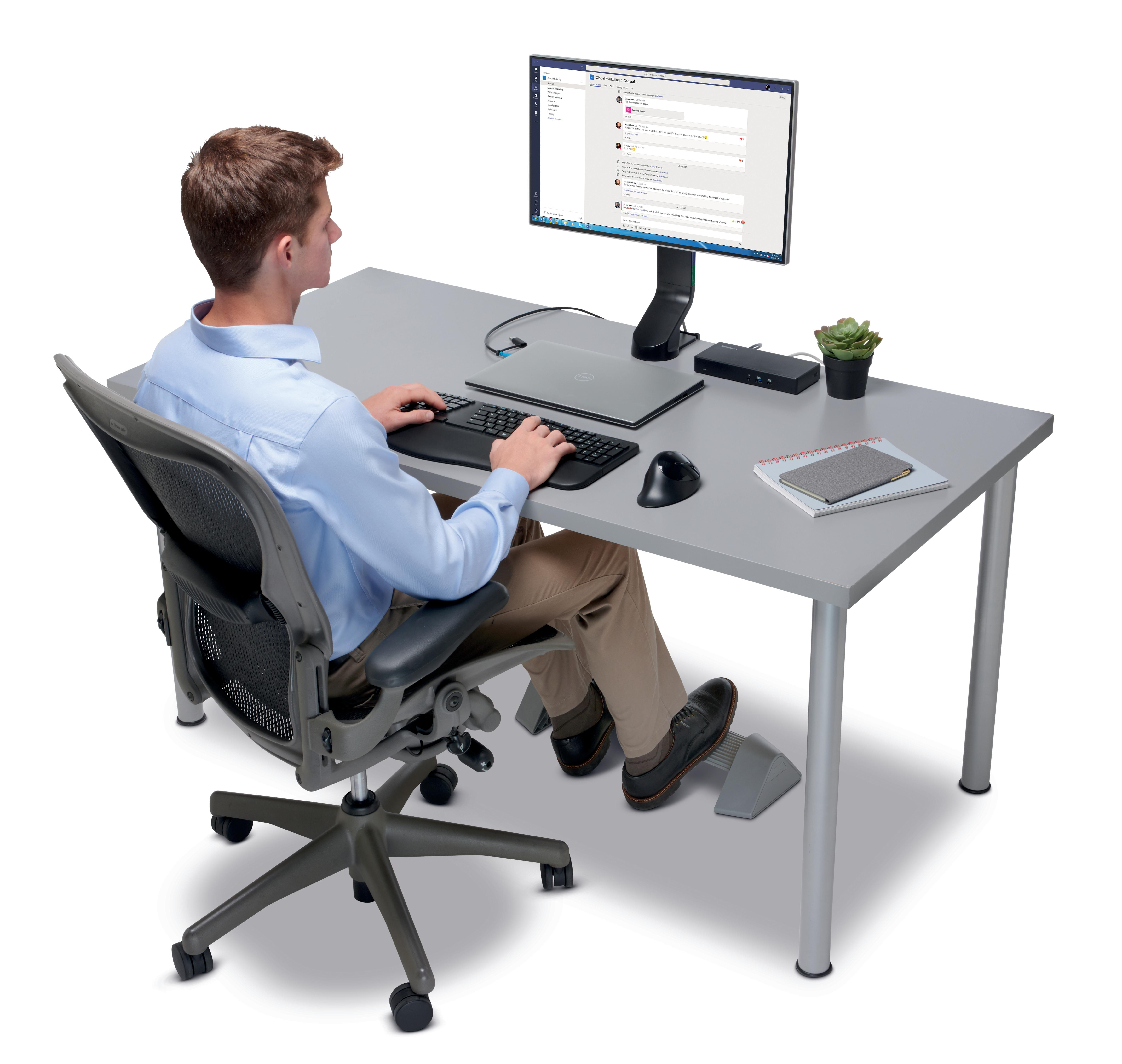 Ein Mann sitzt an einem Schreibtisch und tippt auf einer Tastatur, ein Monitor zeigt eine Messaging-App. Auf dem Tisch eine Maus und Sukkulenten.