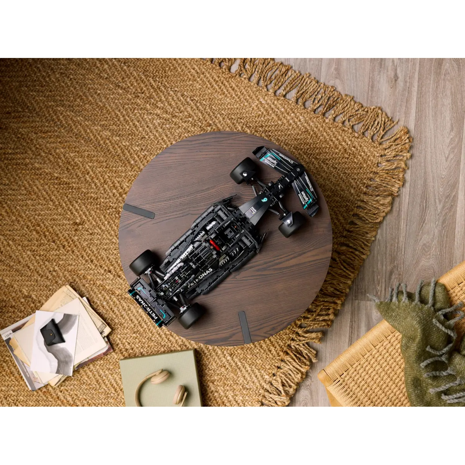 Une voiture de course jouet noire est posée sur une table en bois. La table est sur un tapis tissé. À côté de la table se trouvent des livres, une boîte et des écouteurs.