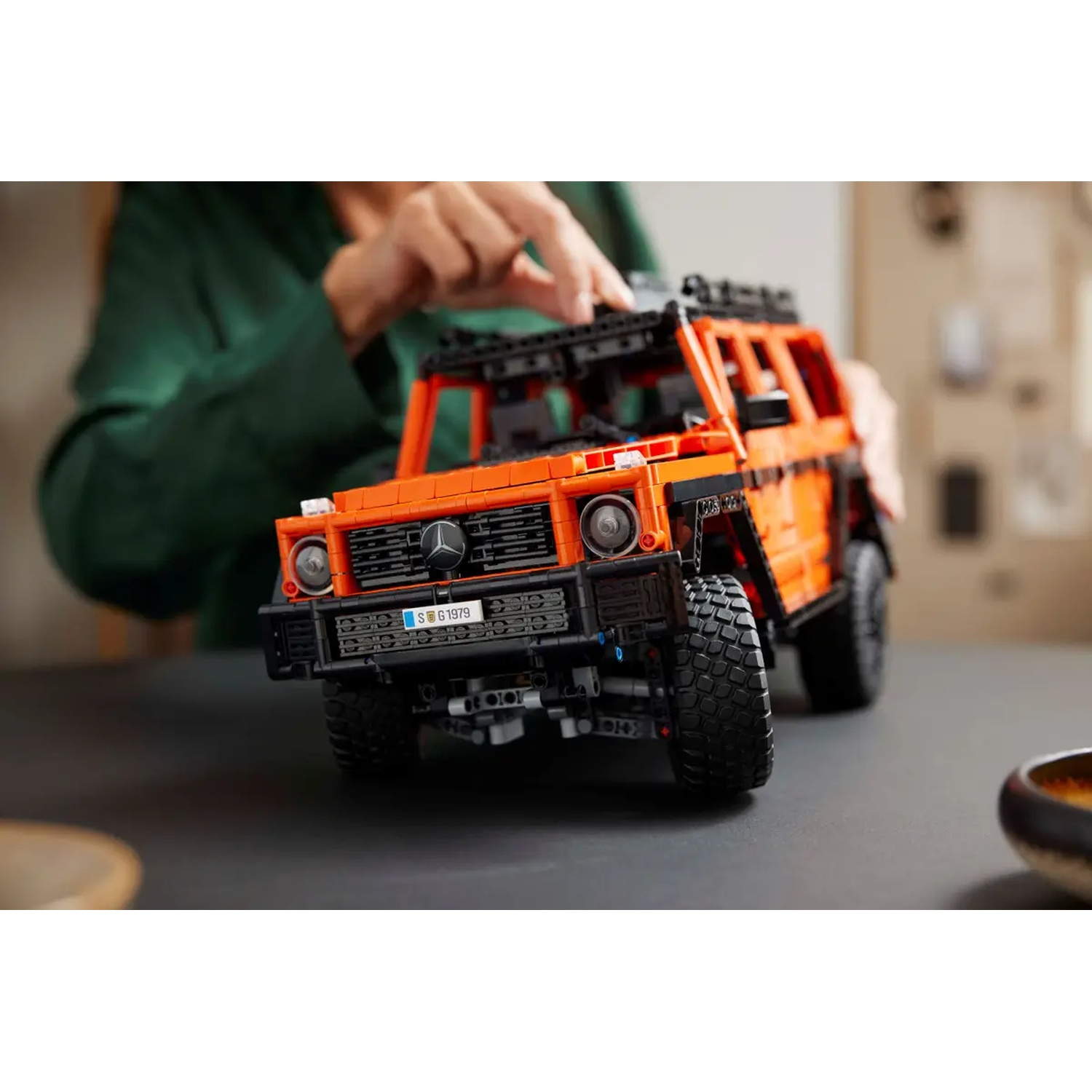 Un modèle Lego orange d'un Mercedes-Benz G-Wagon. Une main est au-dessus de la voiture. La voiture est sur une surface noire.