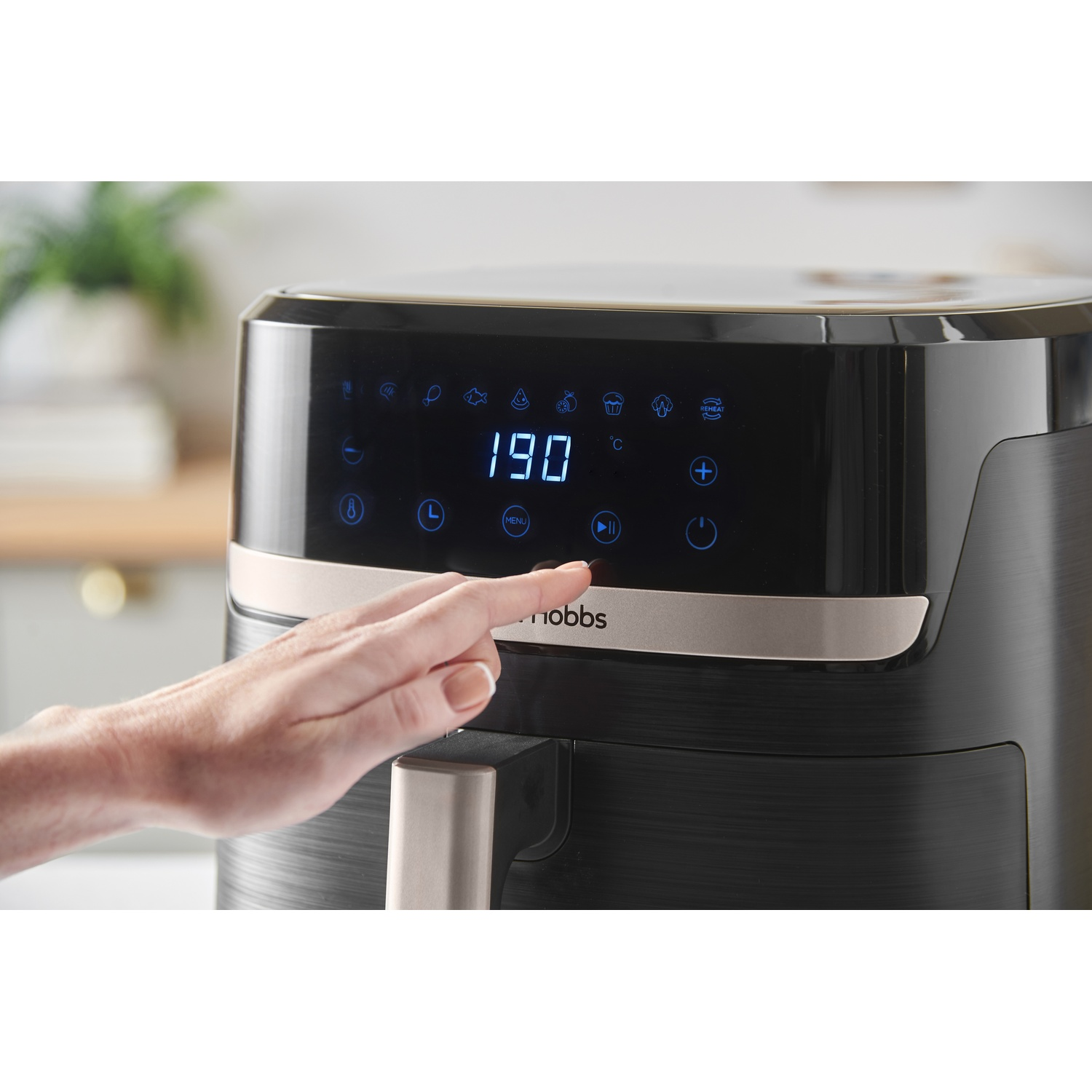 Una mano preme un pulsante su una friggitrice ad aria nera con un display digitale che mostra 190 gradi. Sfondo della cucina.