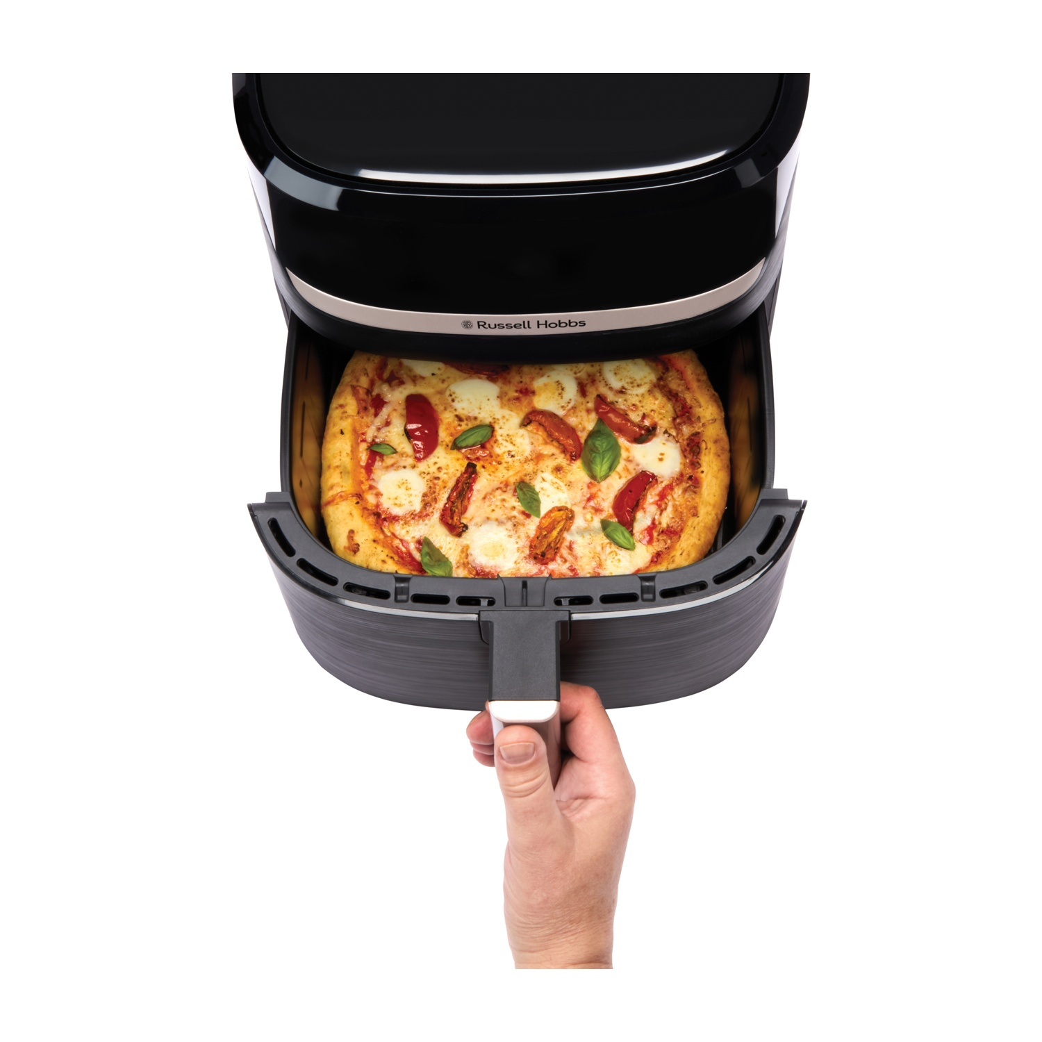 Una friggitrice ad aria con una pizza dentro. Una mano estrae il vassoio. La pizza ha pomodori e basilico. La friggitrice ad aria è nera.
