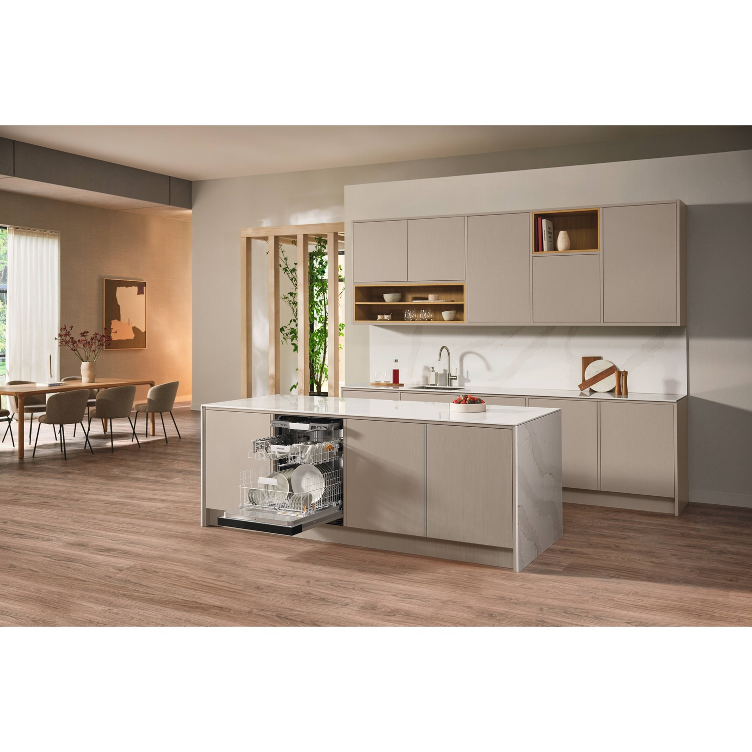 Een moderne keuken met een open vaatwasser, eiland en eethoek op de achtergrond. Beige kasten en houten vloeren.