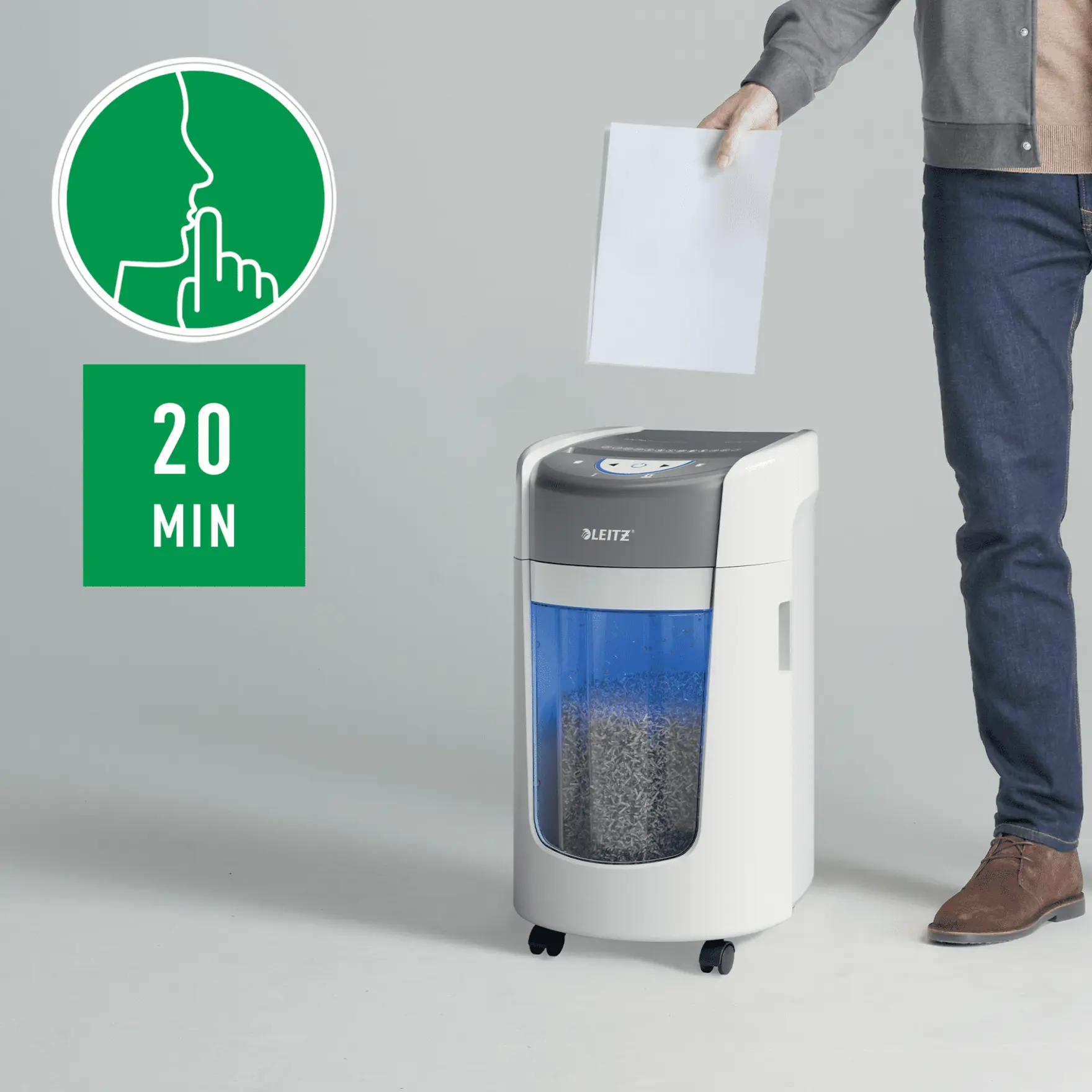 Egy személy fehér papírt adagol egy Leitz iratmegsemmisítőbe. Egy zöld tábla a 'csend' és a '20 perc' feliratot mutatja.