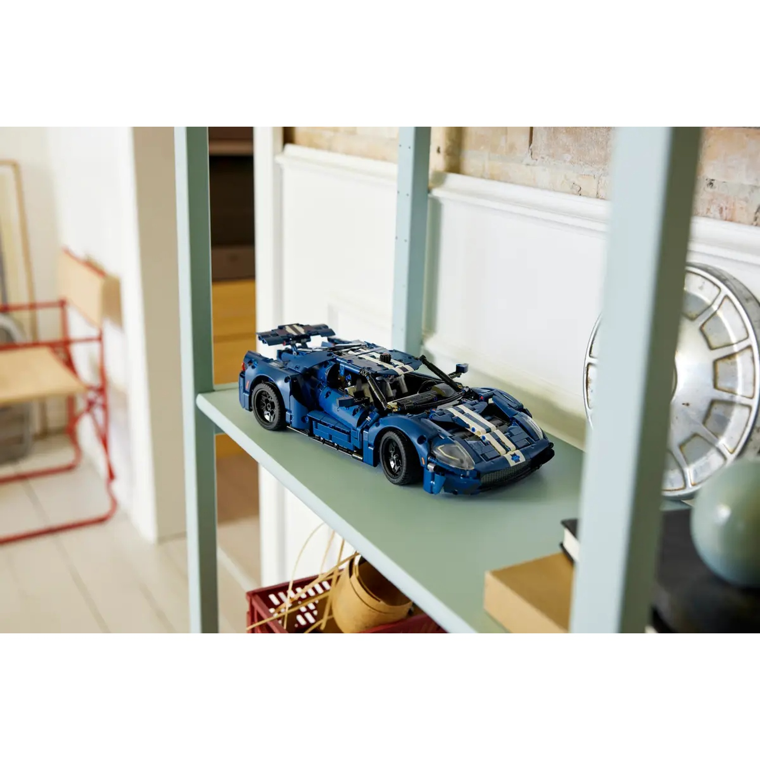 A blue Lego Ford GT car sits on a shelf. Other items include books, a wooden crate, and a metal wheel.