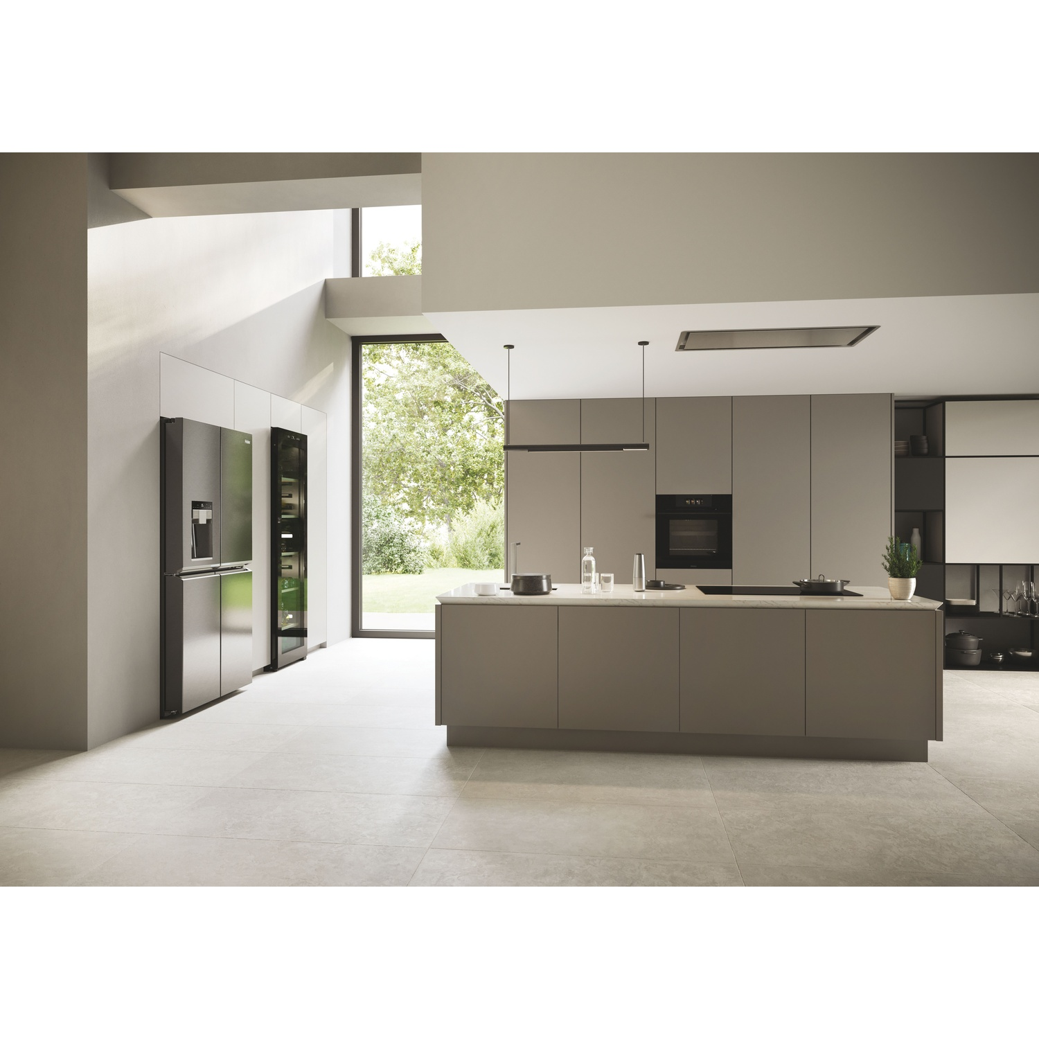 Cucina moderna con elettrodomestici in acciaio inox, isola centrale, ampie finestre con vista giardino e pavimenti e pareti chiare.