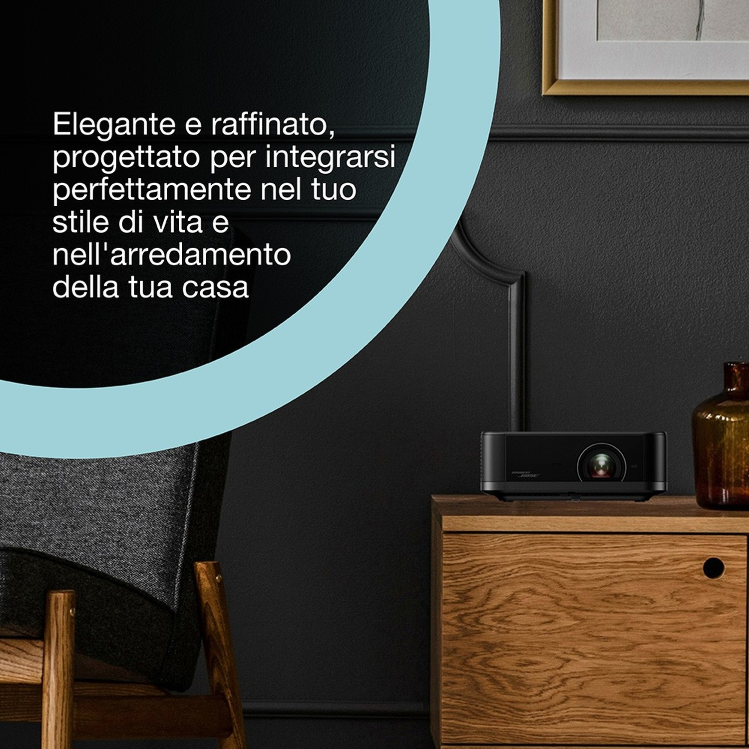 Un proiettore nero è su un mobile di legno, davanti a un muro scuro. Una sedia è a sinistra. Una bottiglia marrone è a destra.