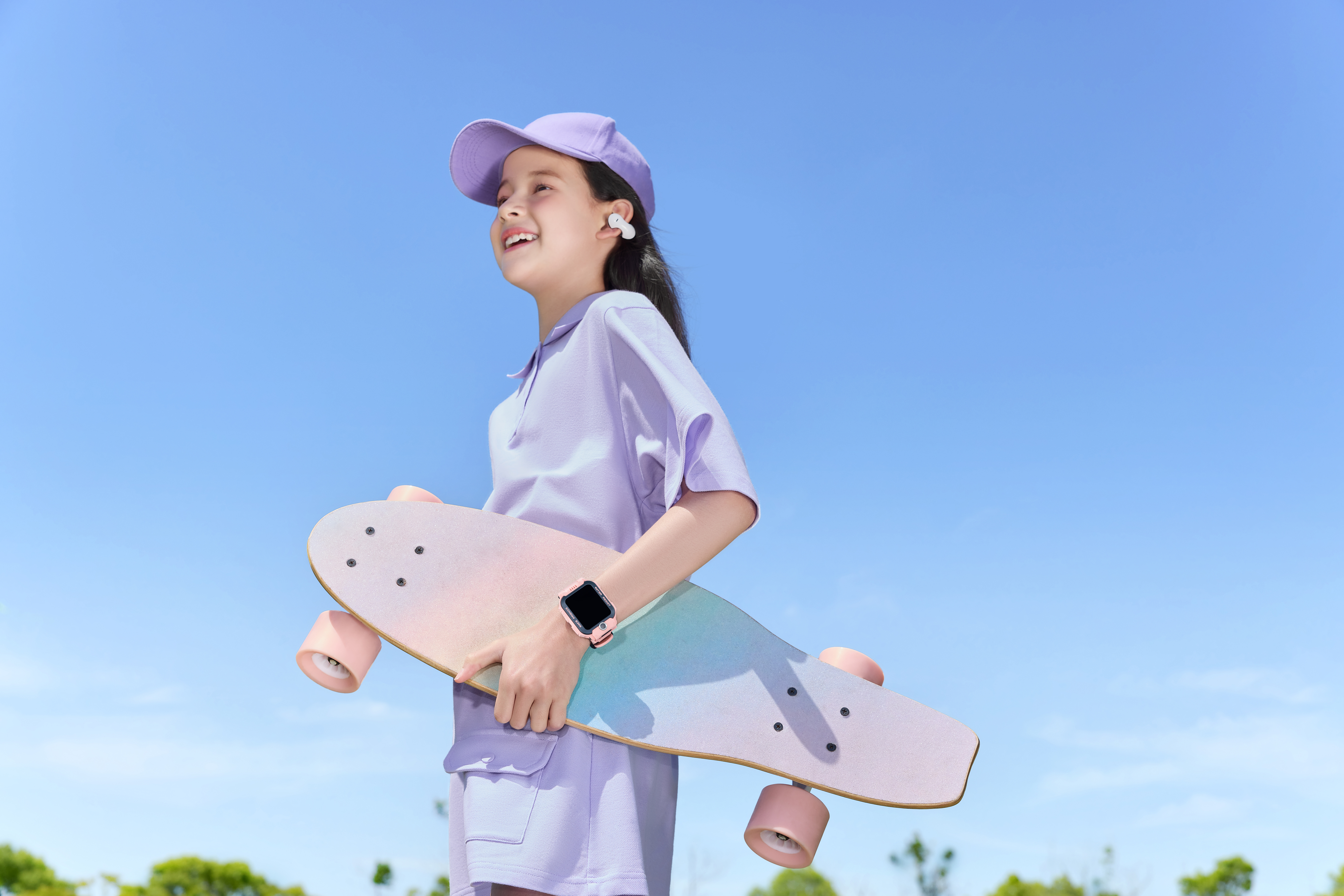 Ein Mädchen in lila Kleidung hält ein Skateboard unter blauem Himmel. Sie trägt Ohrhörer und eine Uhr.