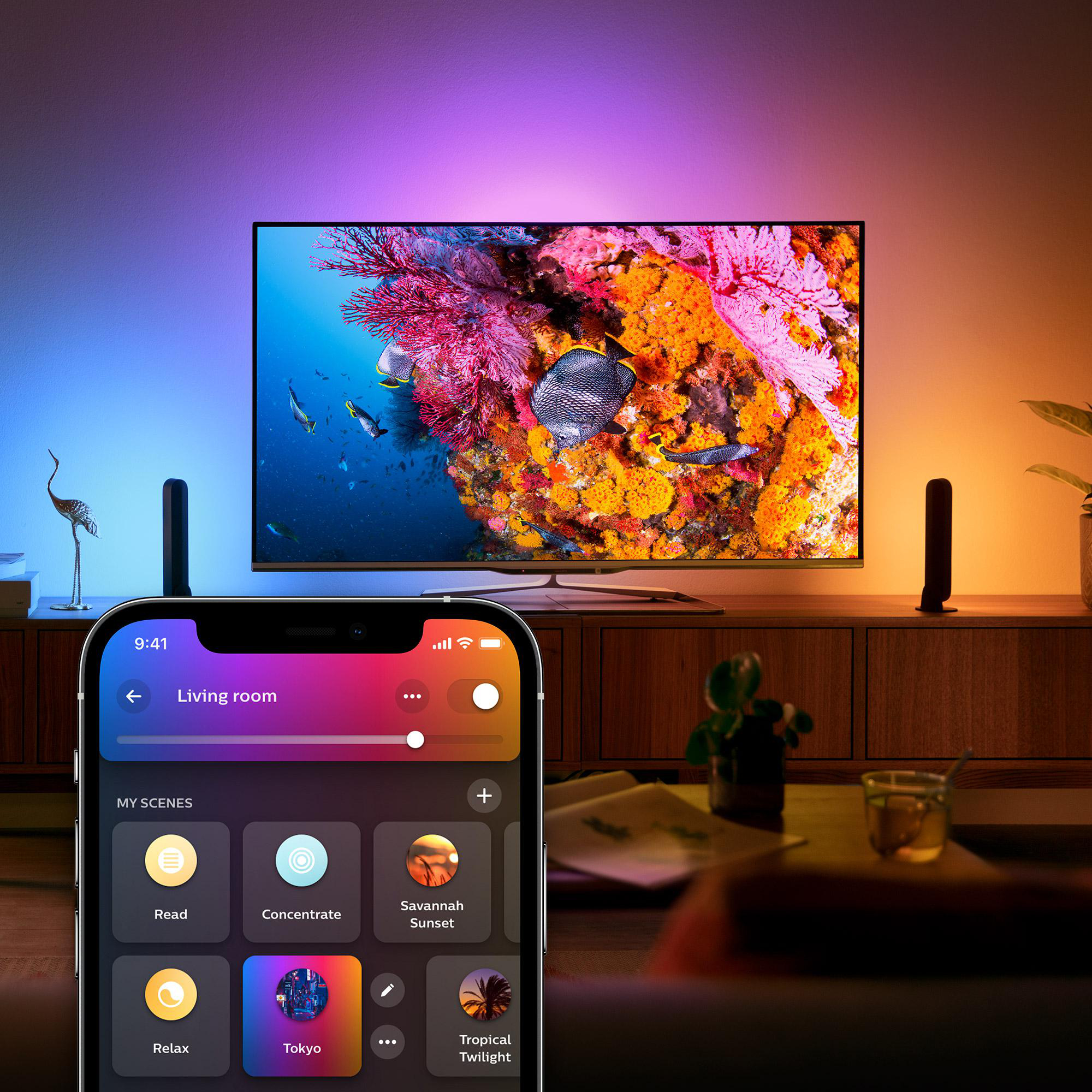 Wohnzimmer-Szene mit TV-Gerät, das Unterwasserleben zeigt, Telefon mit Smart-Home-App und Umgebungslicht.