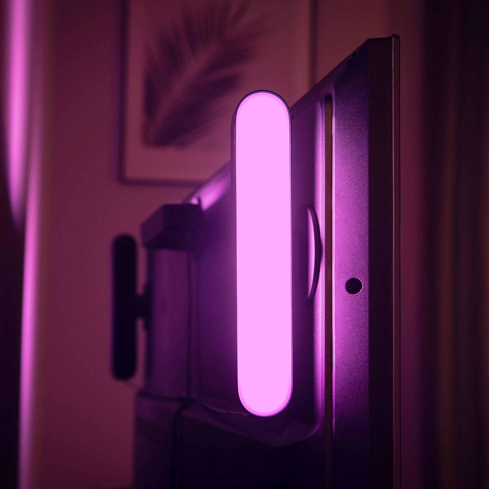 Ein leuchtender, rosa Lichtbalken ist an einem schwarzen Fernseher befestigt. Dunkler Hintergrund mit einem gerahmten Bild.