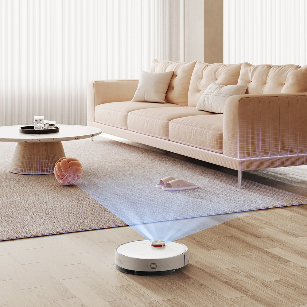 Un robot aspirapolvere pulisce un soggiorno con un divano beige, un tappeto e un tavolino. Pantofole e una palla sono sul tappeto.