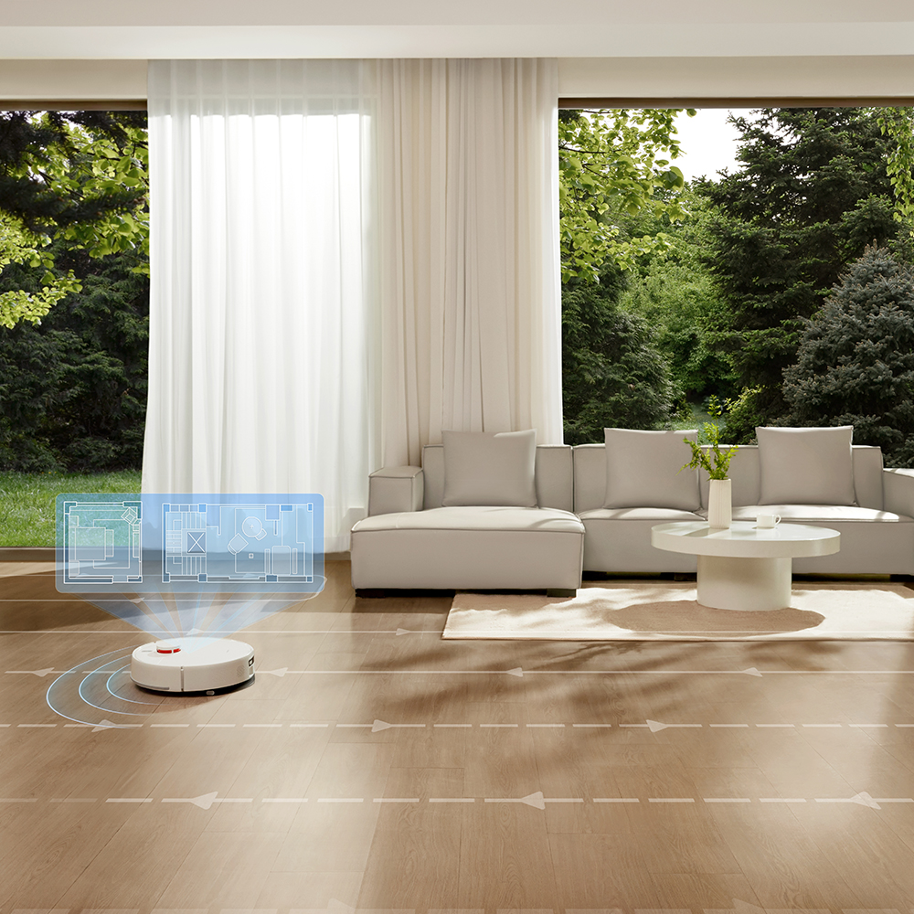 Un aspirapolvere robot bianco sul pavimento in legno che pulisce un soggiorno con divano, tavolo e finestra con vista.