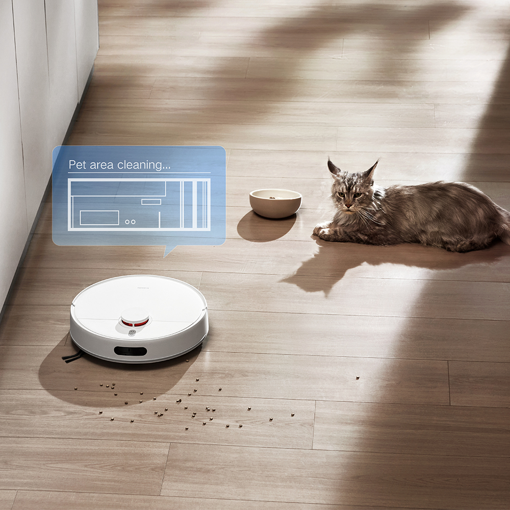 Un aspirapolvere robotico pulisce un pavimento in legno vicino a un gatto sdraiato. Una ciotola è accanto al gatto. L'aspirapolvere è sotto una nuvoletta di testo.