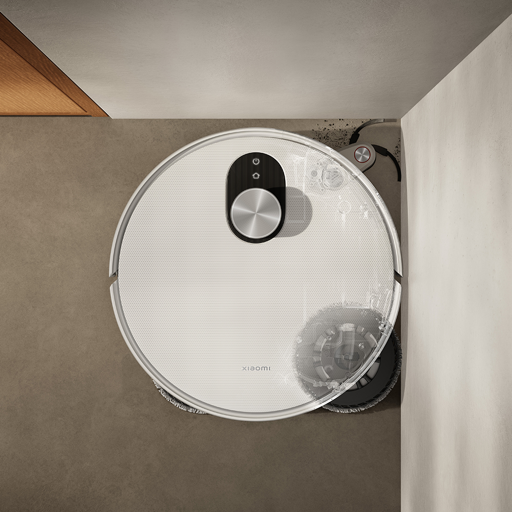 Vue aérienne d'un aspirateur robot Xiaomi blanc. Il nettoie un sol carrelé marron, à côté d'un mur.