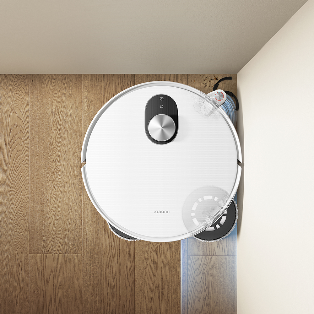 Un aspirateur robot blanc sur un plancher de bois nettoyant à côté d'un mur blanc. L'aspirateur est près d'un coin.