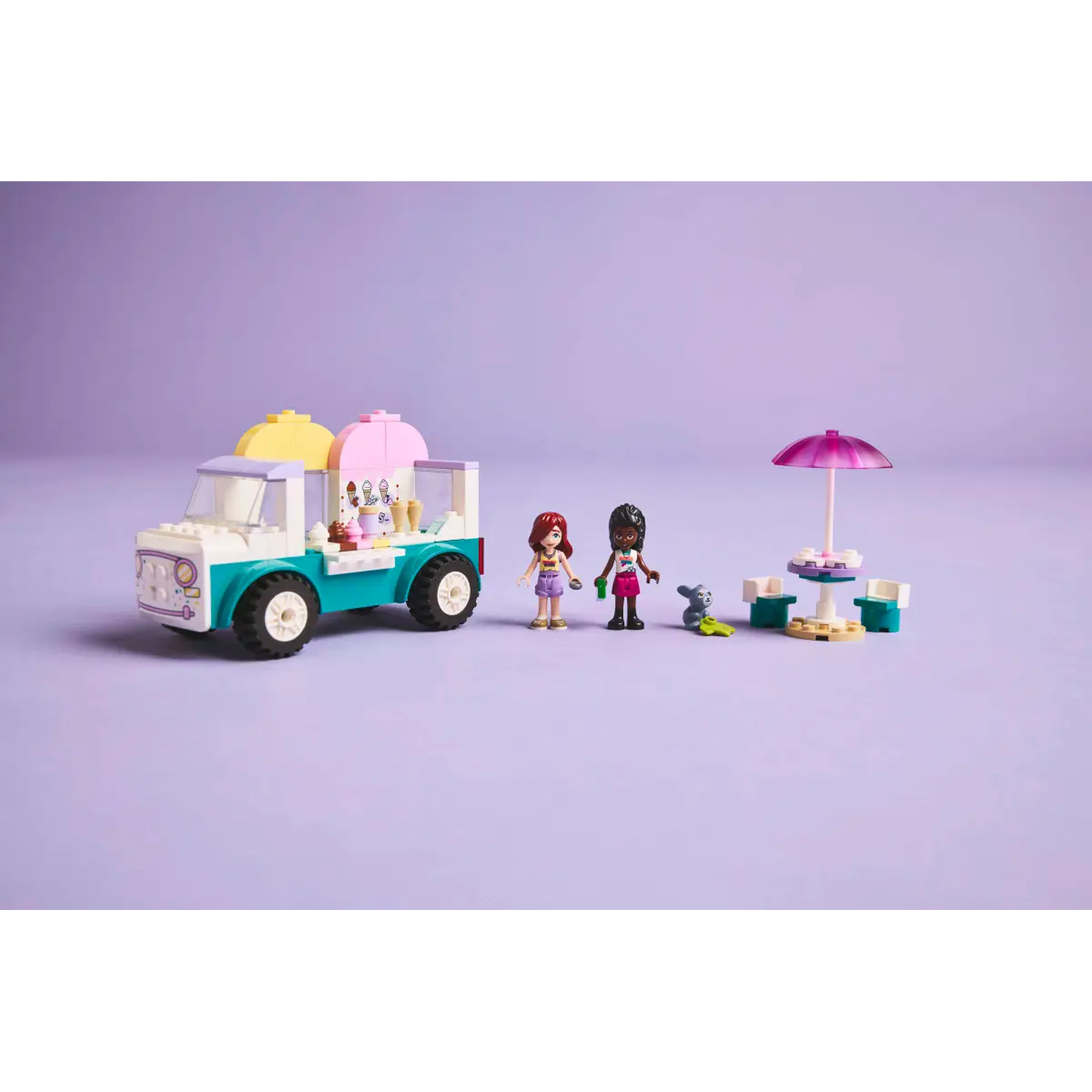 Lego set met een ijsjeswagen, twee Lego figuren, een tafel met parasol en een klein dier, alles op een paarse achtergrond.