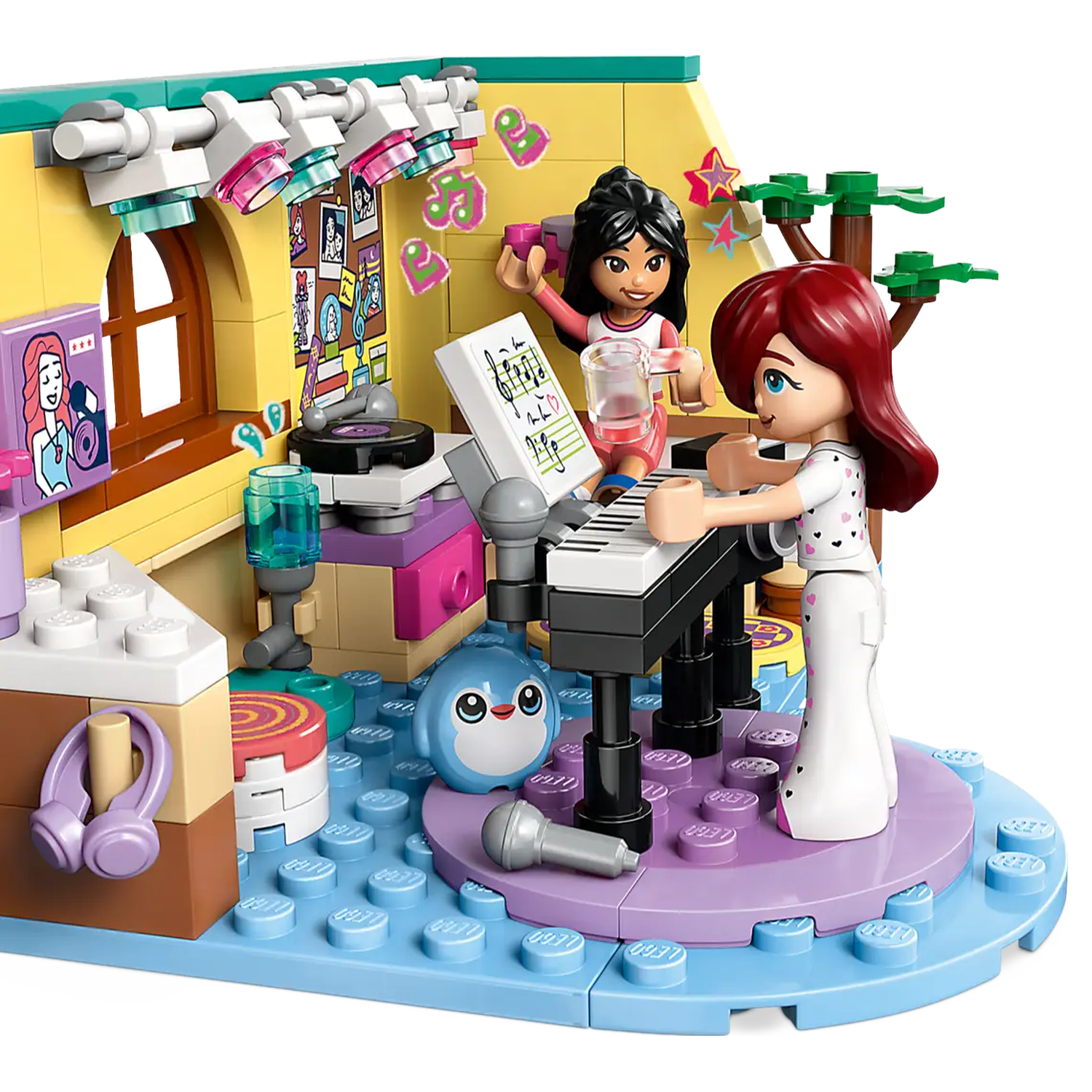 Lego set depicting two girls playing music. One plays a keyboard, other holds a drink. Stage with penguin, microphone, and lights.