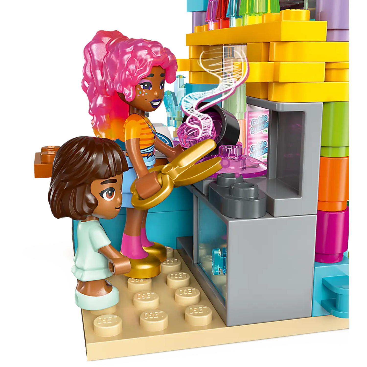 Two Lego figures with pink and brown hair, use golden scissors in a lab. Background has colorful blocks and a counter.