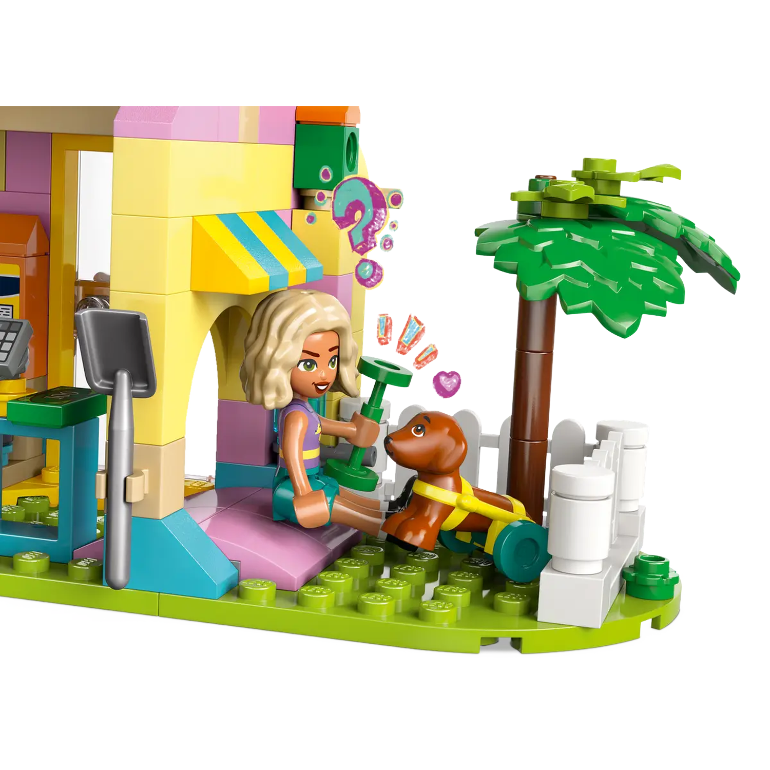 Lego set with a girl, a dog with wheels, and a building with a palm tree. The girl is holding a green object.