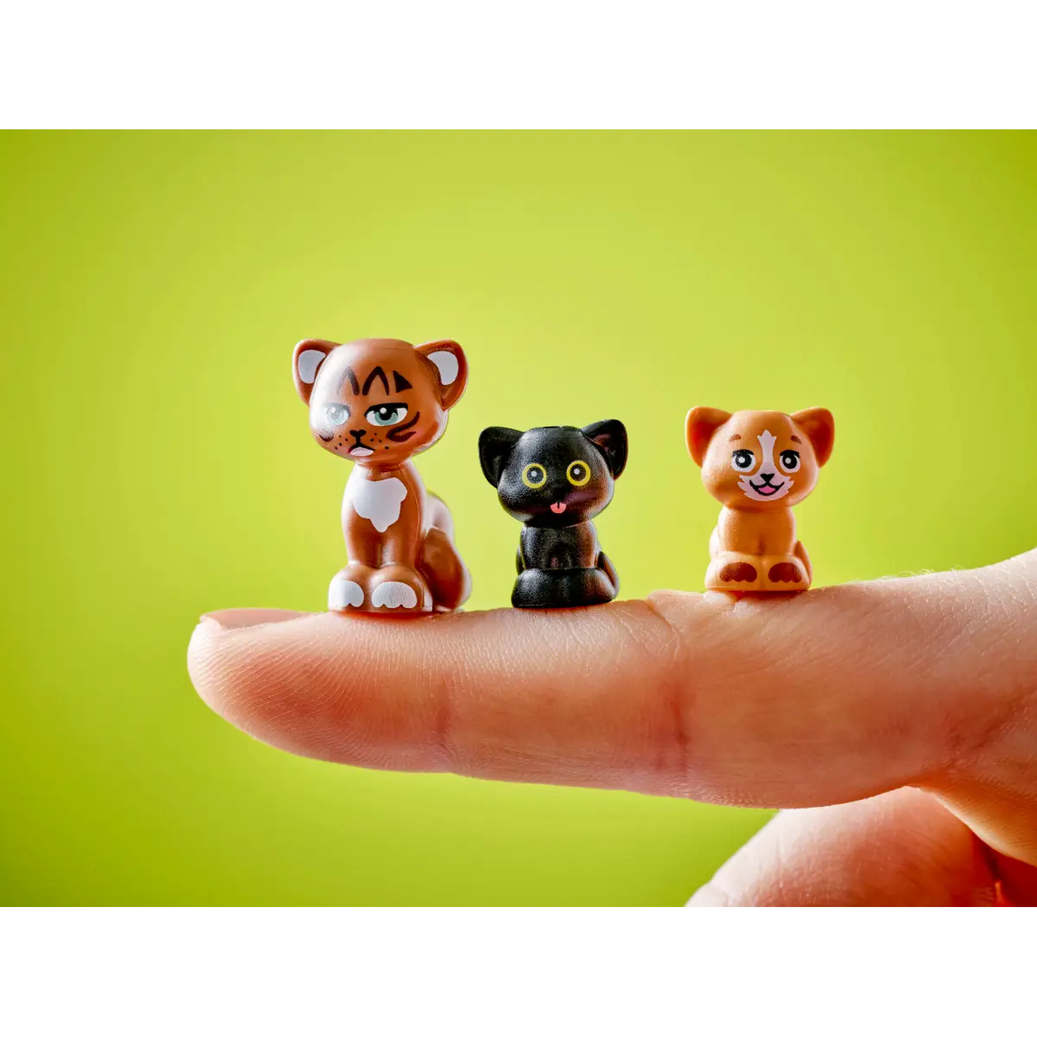 Three toy animal figures on a finger. A brown lion, a black cat, and an orange lion cub, set against a green background.
