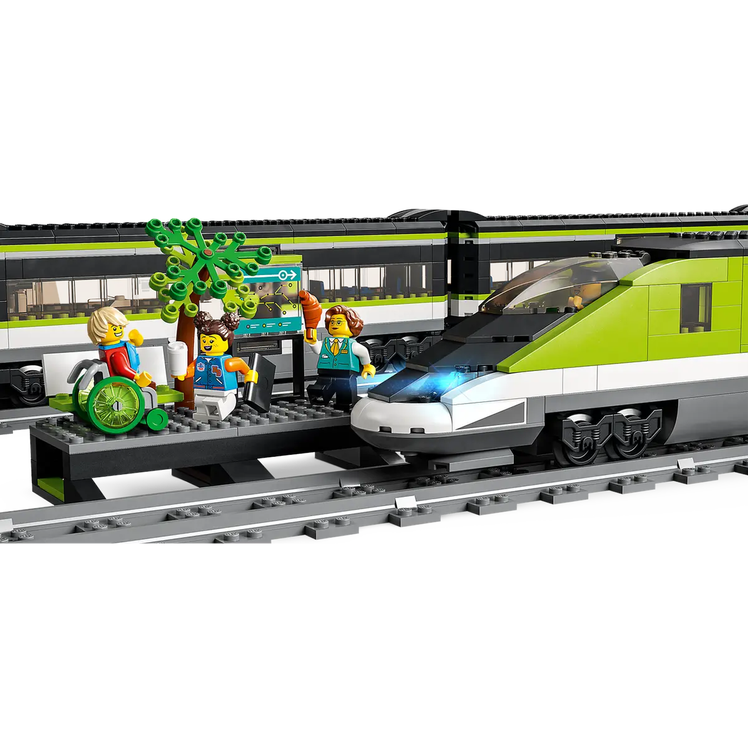Lego-treinset met figuren. Groene en zwarte trein op rails. Mensen op een station, één in een rolstoel. Boom en bord.