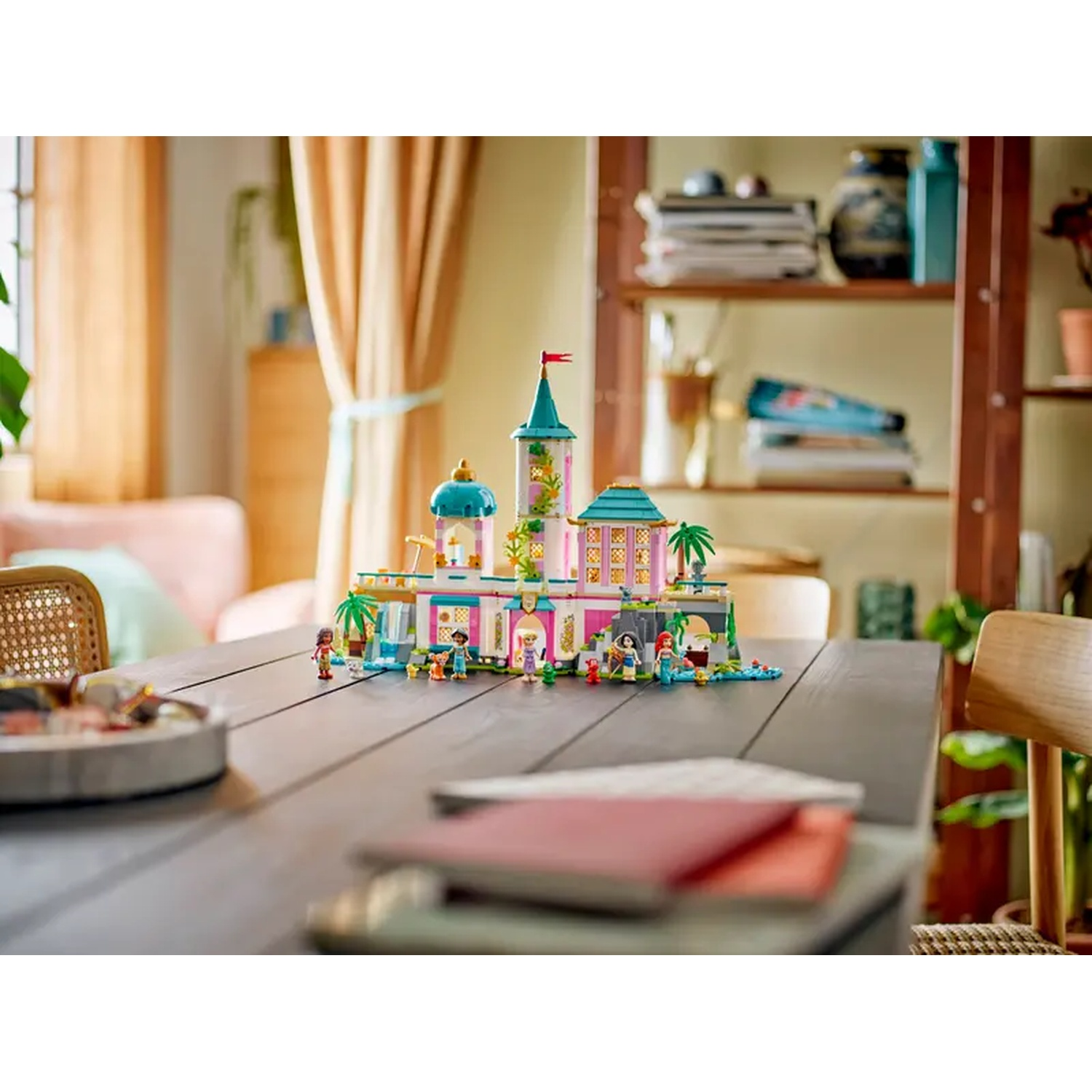 Een Lego Disney kasteel speelset op een tafel. Figuren en accessoires zijn gerangschikt. Achtergrond toont een kamer met planken en gordijnen.