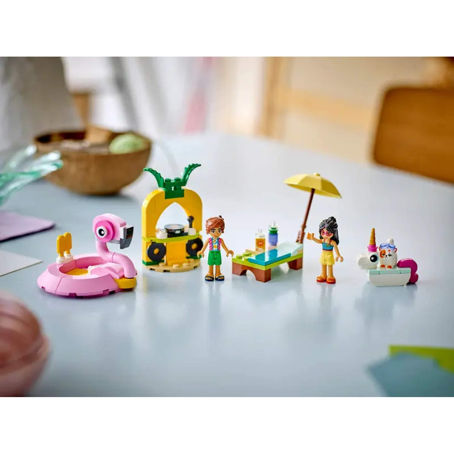 Lego set with figures and accessories. A flamingo float, pineapple stand, table, umbrella, unicorn float, and two figures are visible.