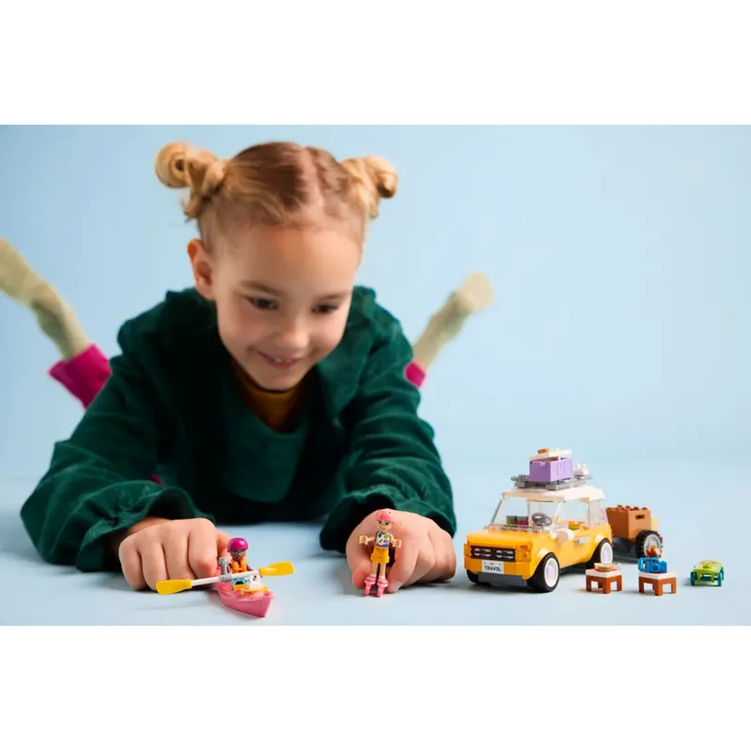 A girl plays with Lego Friends set. Yellow car, pink kayak, and mini figures are on a blue background.
