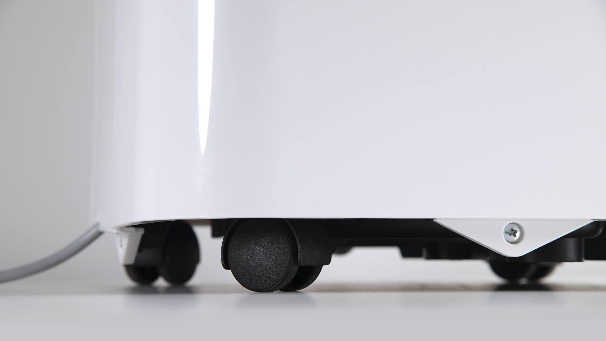 Zbliżenie białego urządzenia z czarnymi kołami na białej powierzchni. Szary kabel wychodzi z boku.