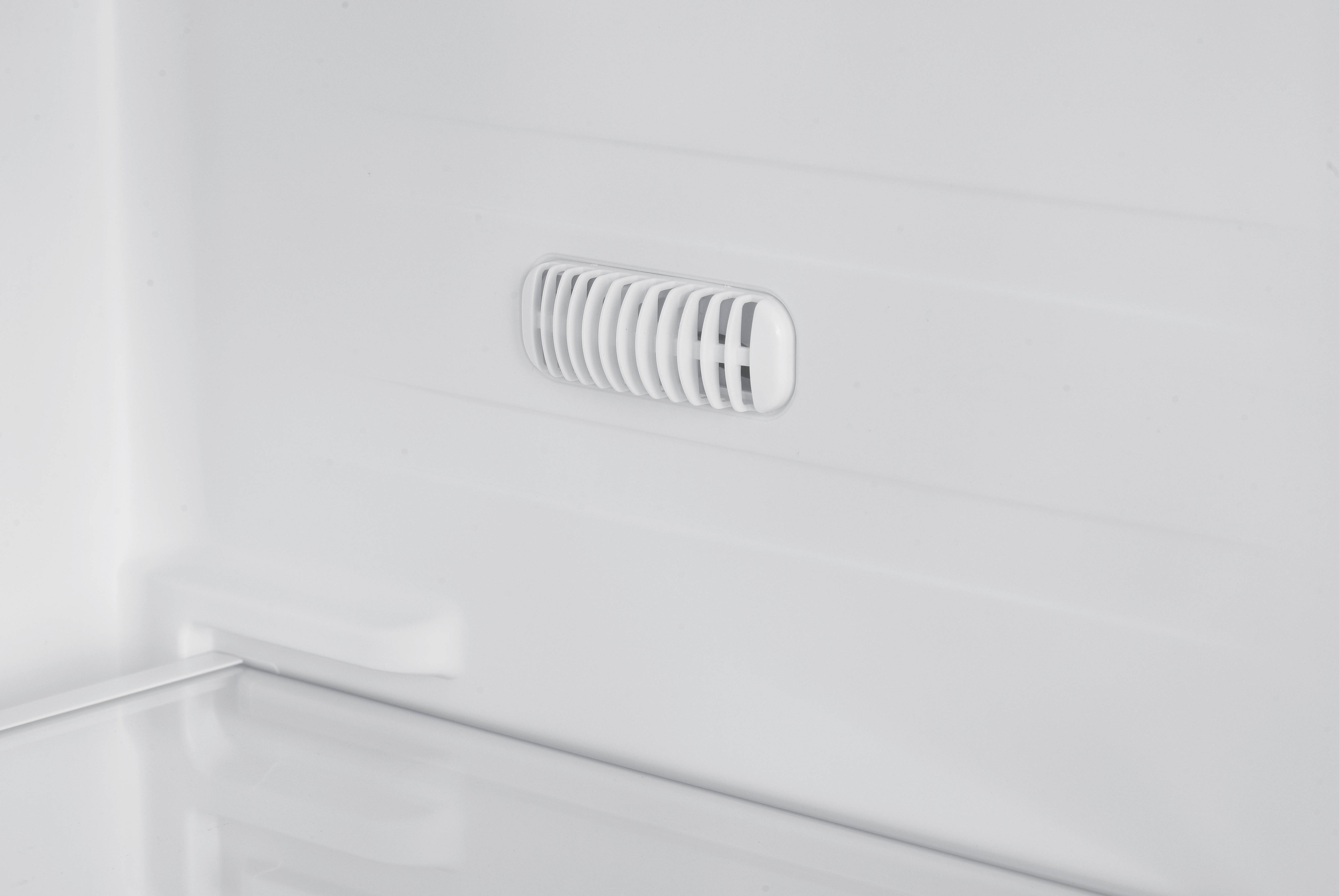Wnętrze białej lodówki. Biały otwór wentylacyjny pośrodku z pionowymi listwami.