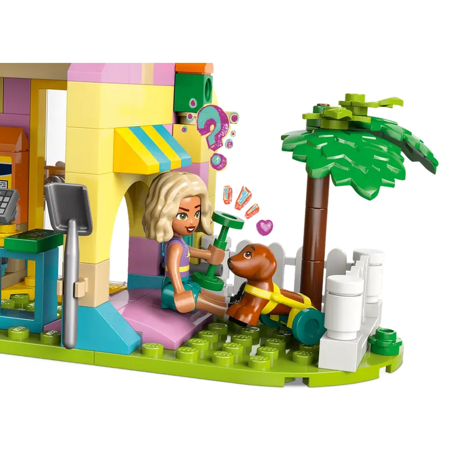 A Lego scene shows a girl with a dog. There's a building and a tree. The dog has a harness and wheels.