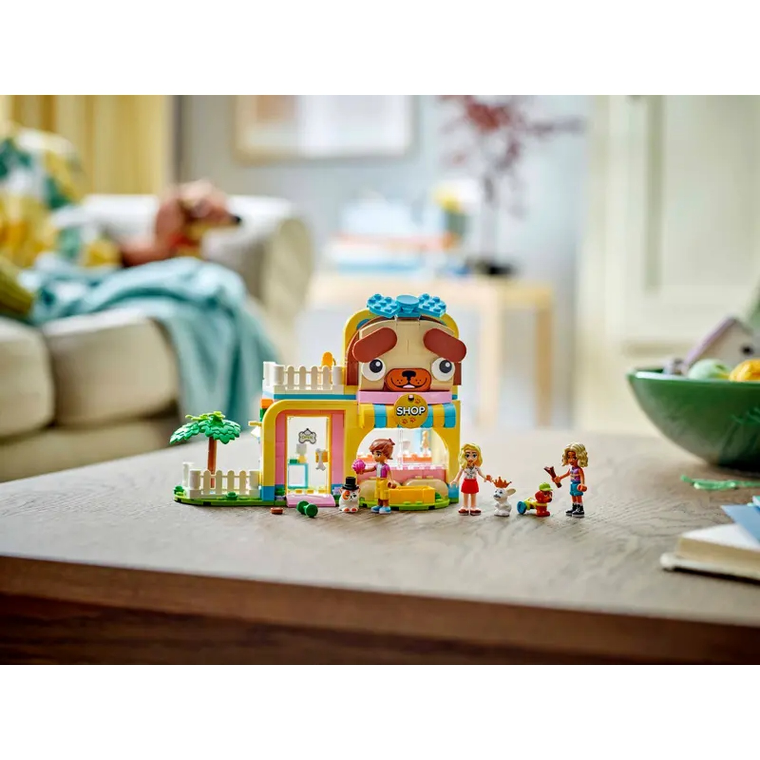 A Lego dog shop with figures, a dog, and vegetables. A person is sitting on a sofa in the background.