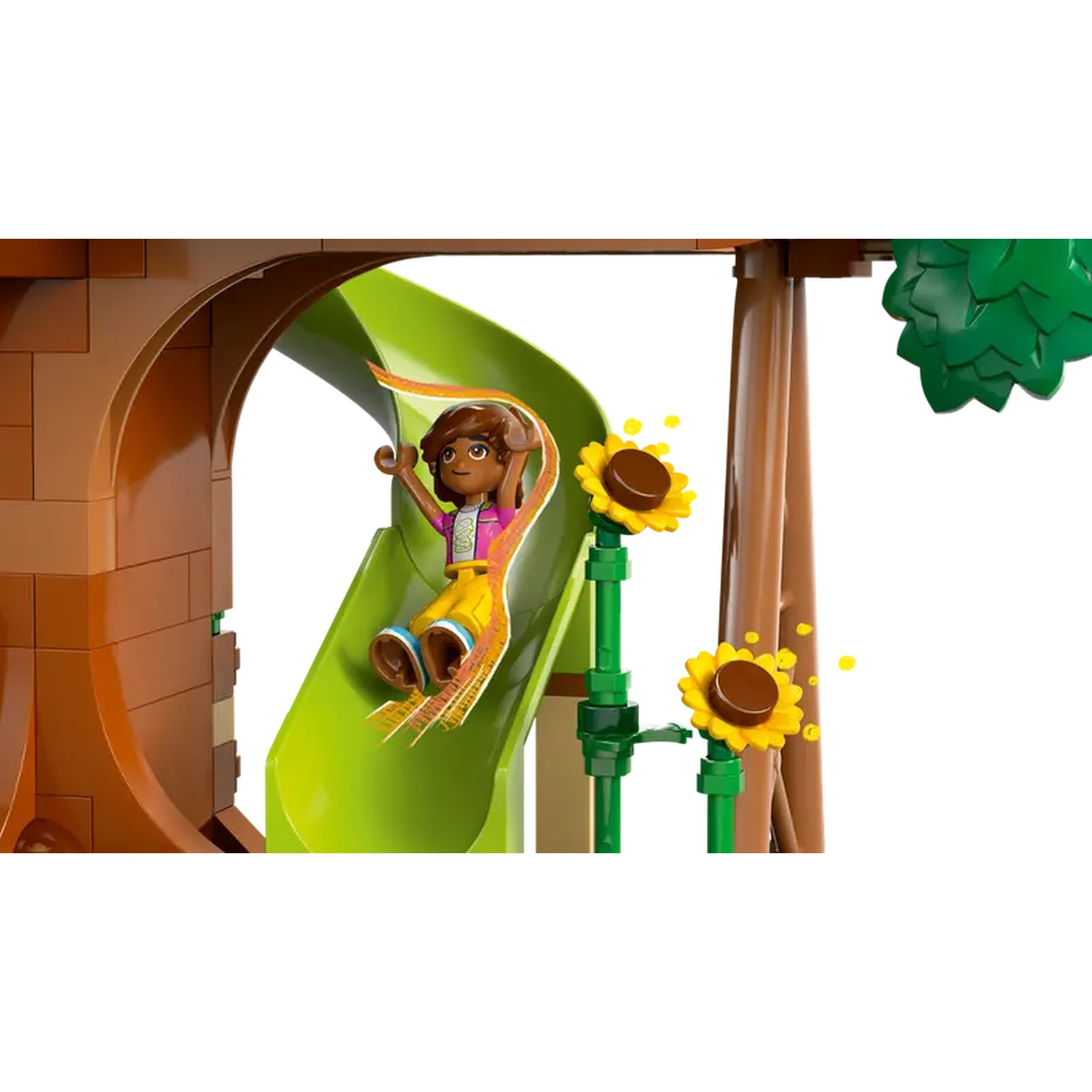 Une figurine Lego glisse sur un toboggan vert. Des tournesols et un arbre sont également visibles. Le fond est blanc.
