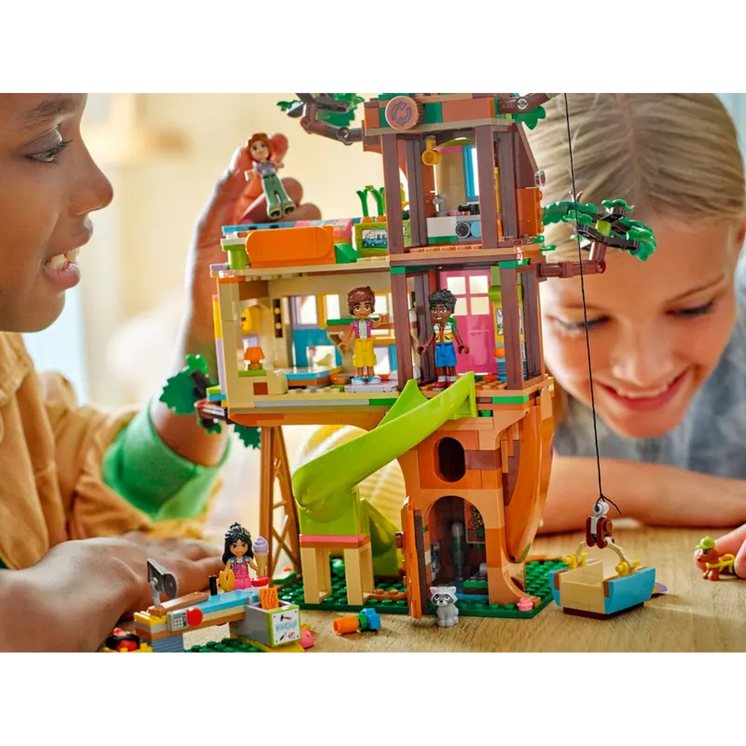 Deux enfants jouent avec un ensemble de cabane dans les arbres Lego. L'ensemble comprend des figurines, un toboggan et d'autres accessoires.