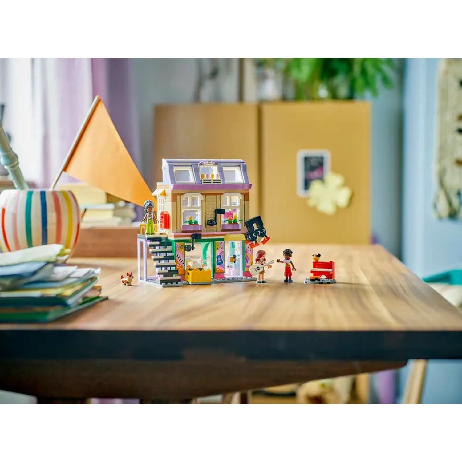 Een Lego-set op een houten tafel. Het bevat een gebouw met minifiguren en diverse accessoires. Een vlag en een gestreepte beker zijn ook zichtbaar.