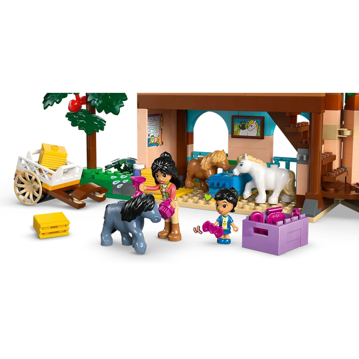 Een Lego paardenstal scène met figuren, paarden en accessoires. Er is een wagen, een boom en een doos met roze items.