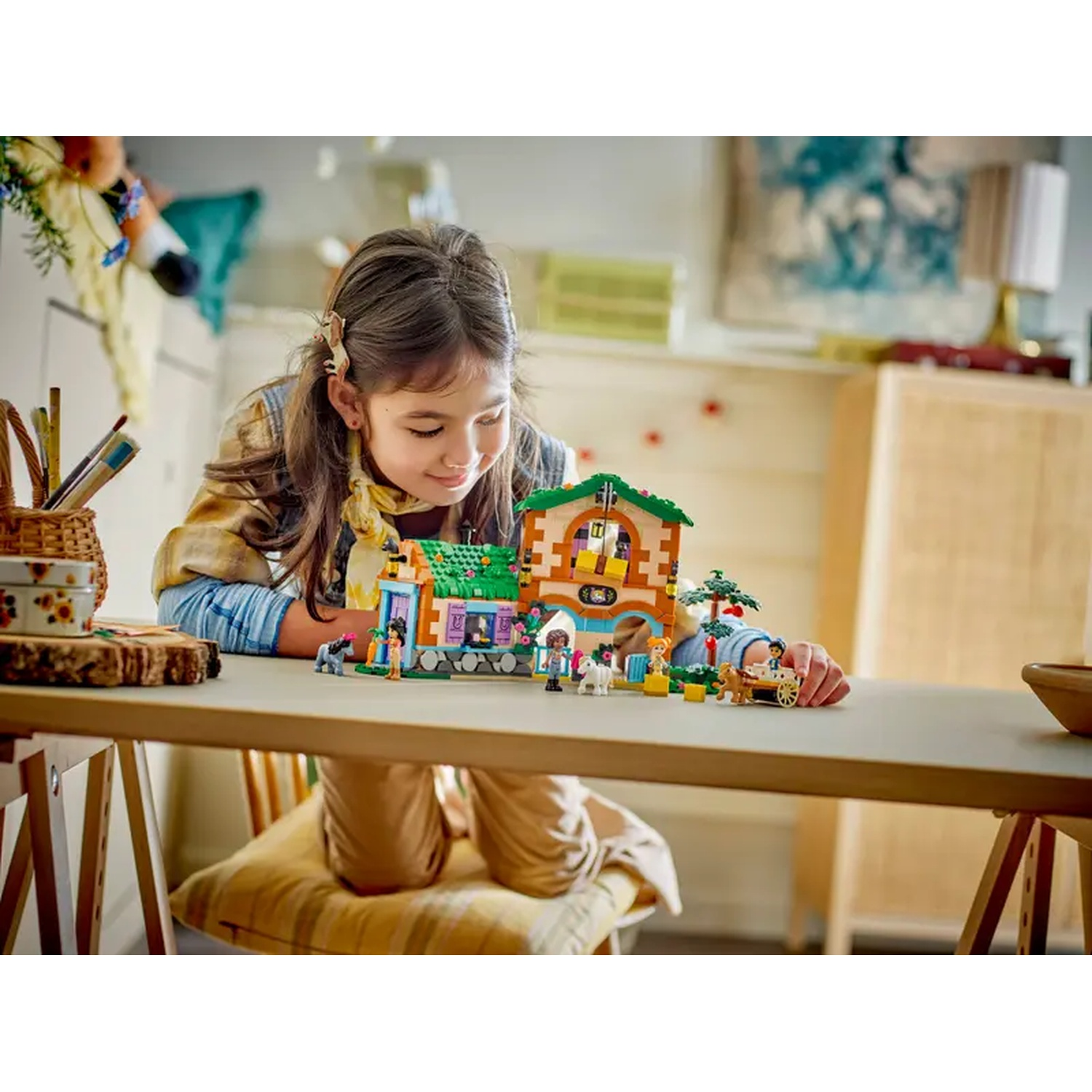 Een meisje speelt met een Lego-set van een huis. Ze zit aan een tafel met de Lego-set voor zich.