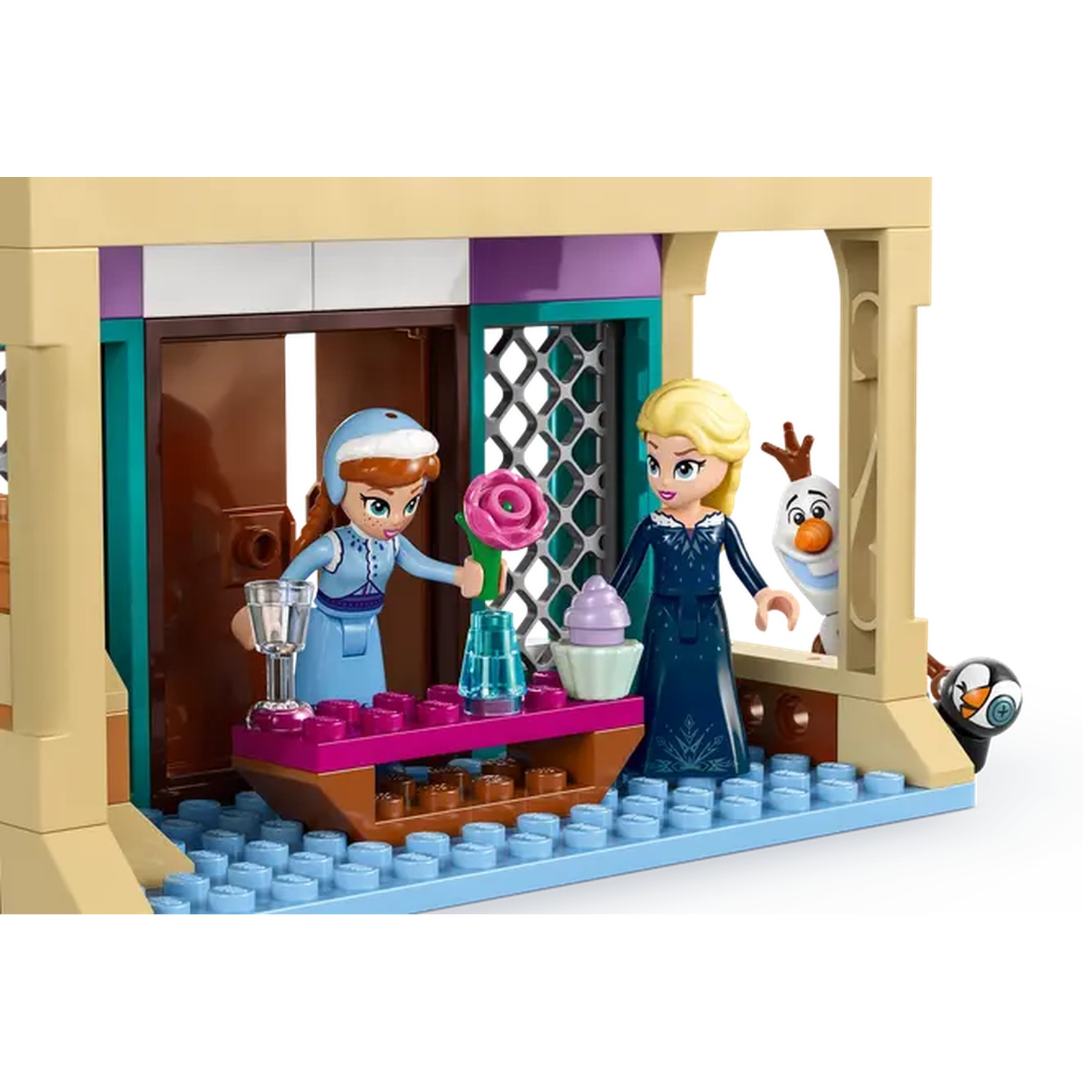 Lego set met Anna, Elsa, Olaf en een pinguïn. Anna houdt een roos vast. Elsa staat bij een cupcake. Tafel met drankje en vaas.