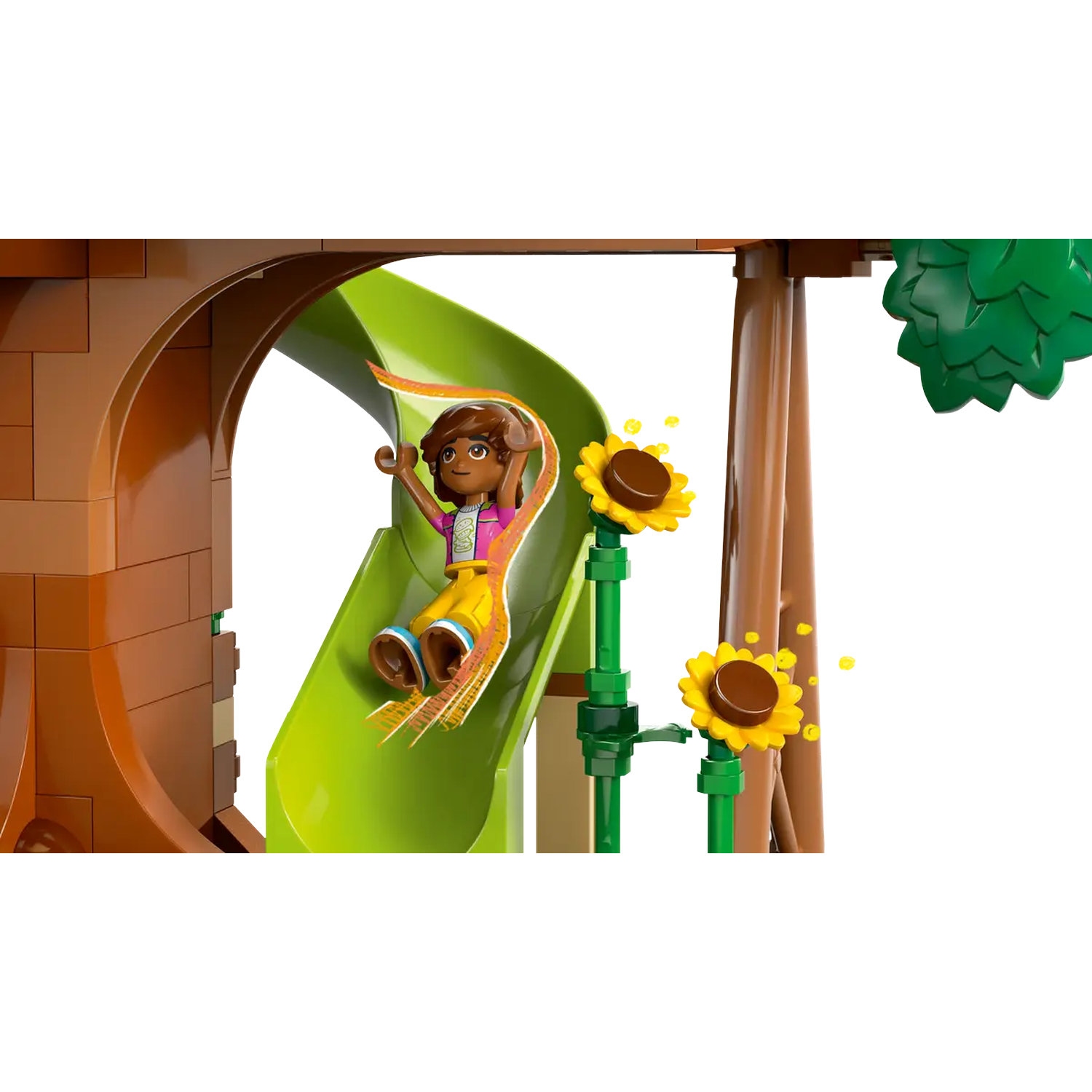 A Lego figure slides down a green slide. Sunflowers and a tree structure are in the background. The figure is wearing yellow pants.
