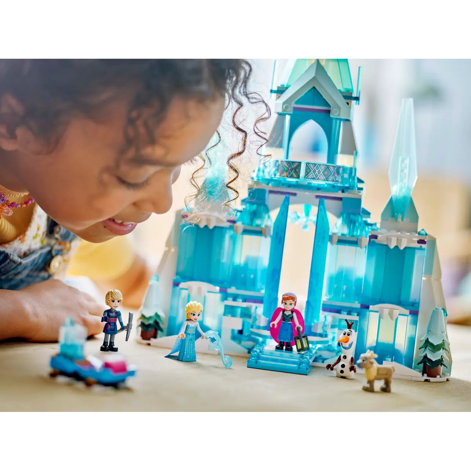 Een kind bekijkt een LEGO Frozen-kasteel. Elsa, Anna, Olaf, Kristoff en Sven figuren staan voor het kasteel.